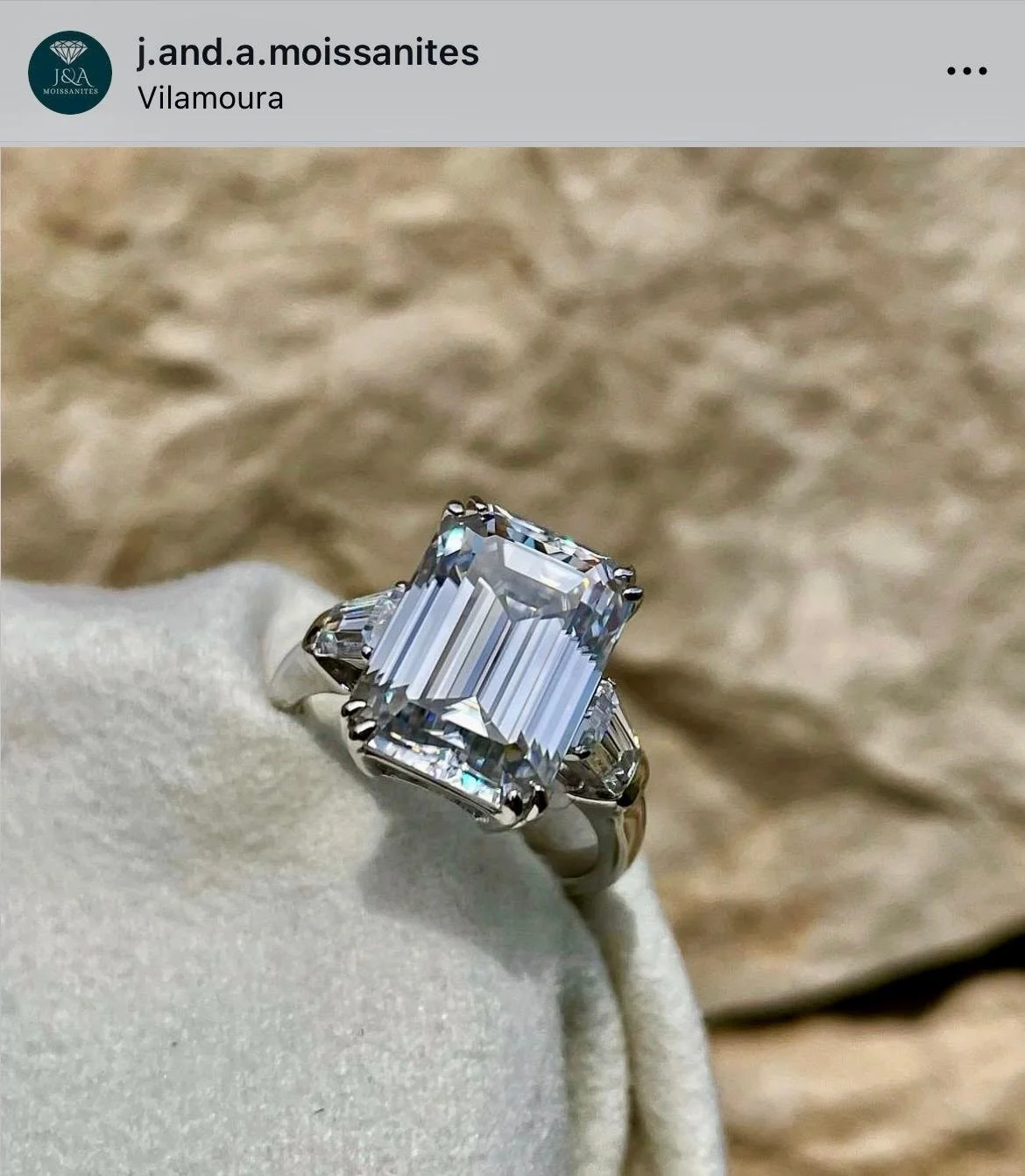 A large rectangular cut diamond ring with a band, resting on a beige fabric background.