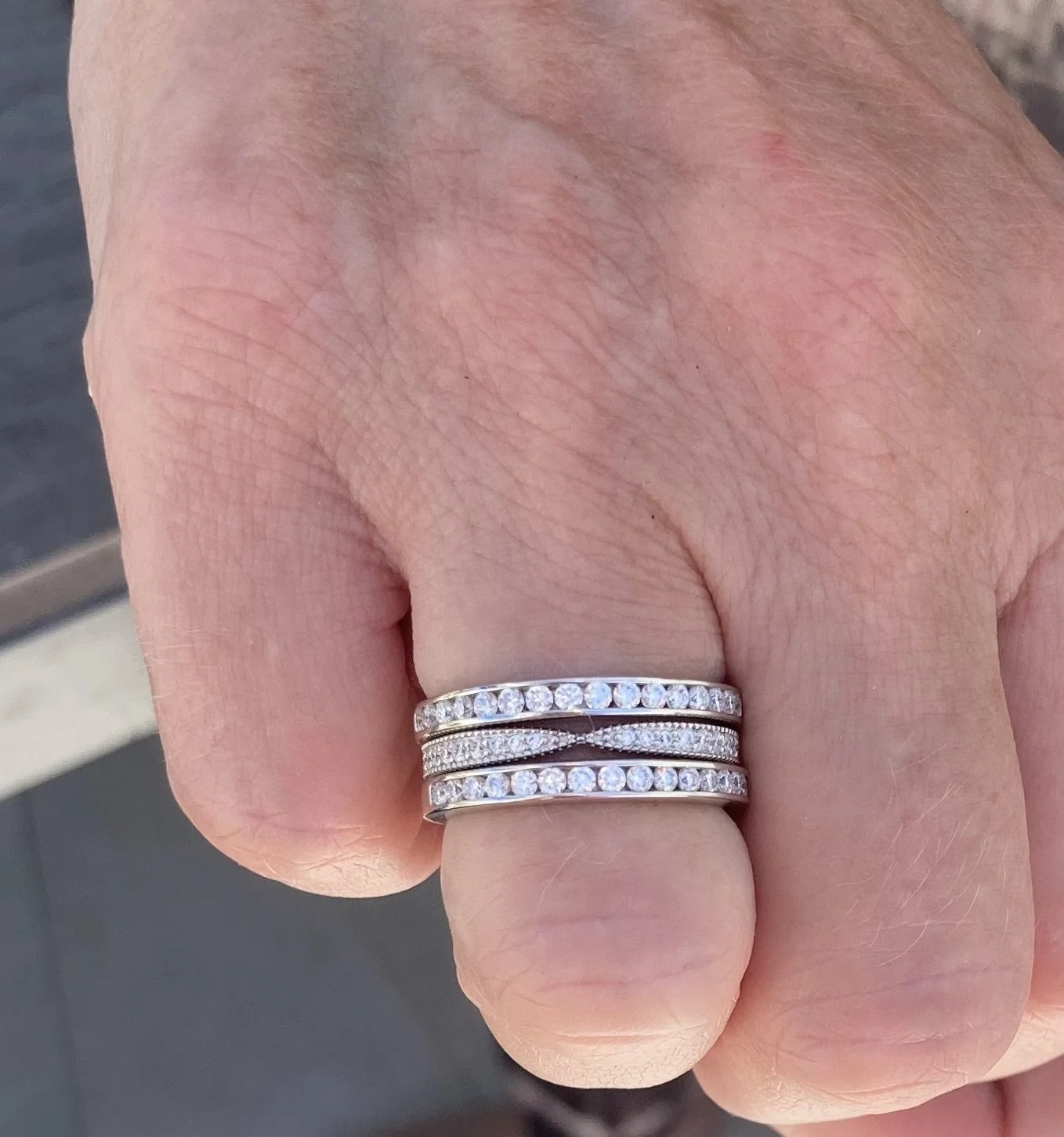 Close-up of a hand wearing multiple silver rings with clear gemstones, including what appears to be a wedding or engagement ring with a row of diamonds.