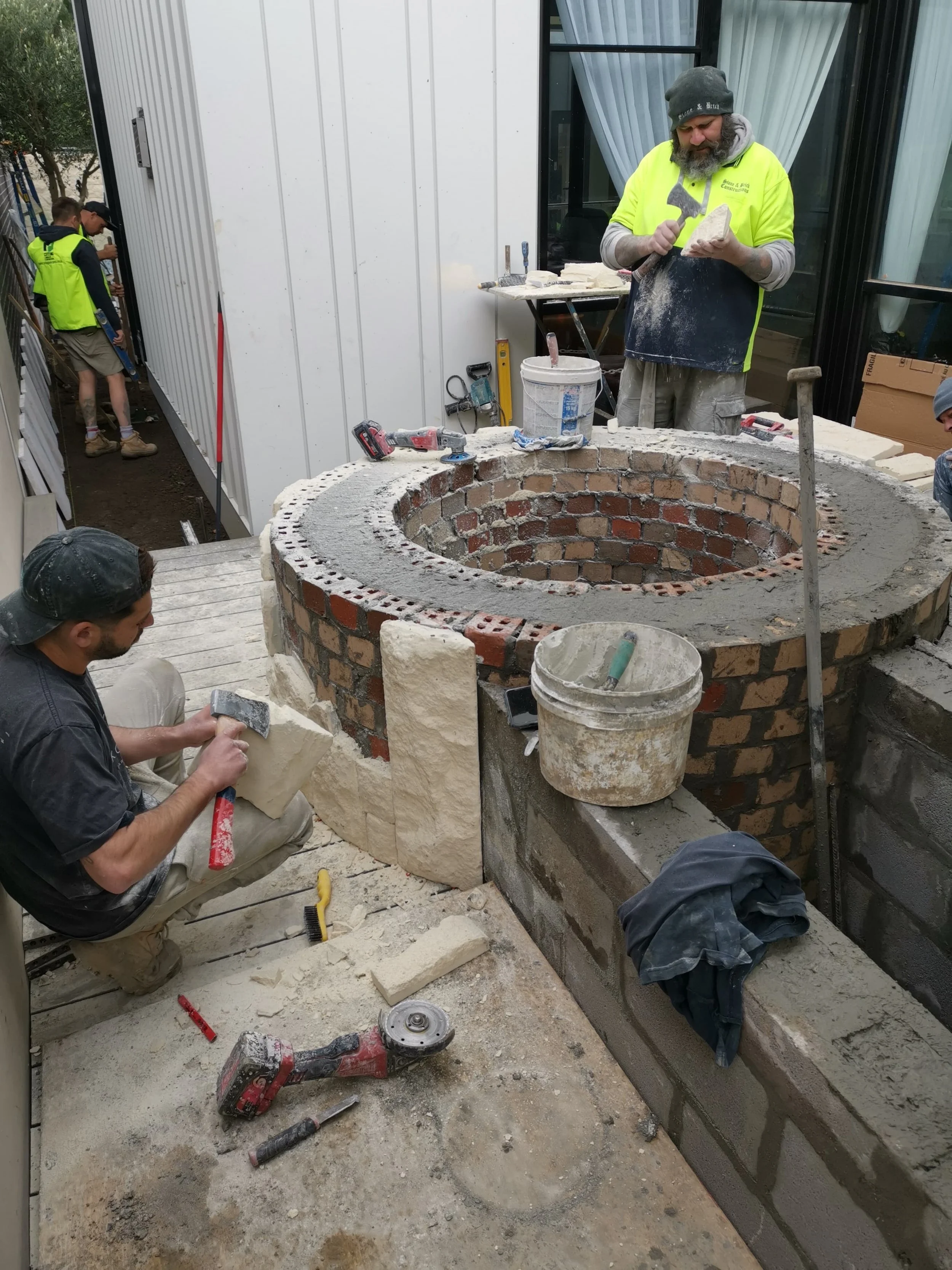 The Block 2020, Exotic Living. Tradesmen building a circular brick outdoor planter box, with tools and materials around them.