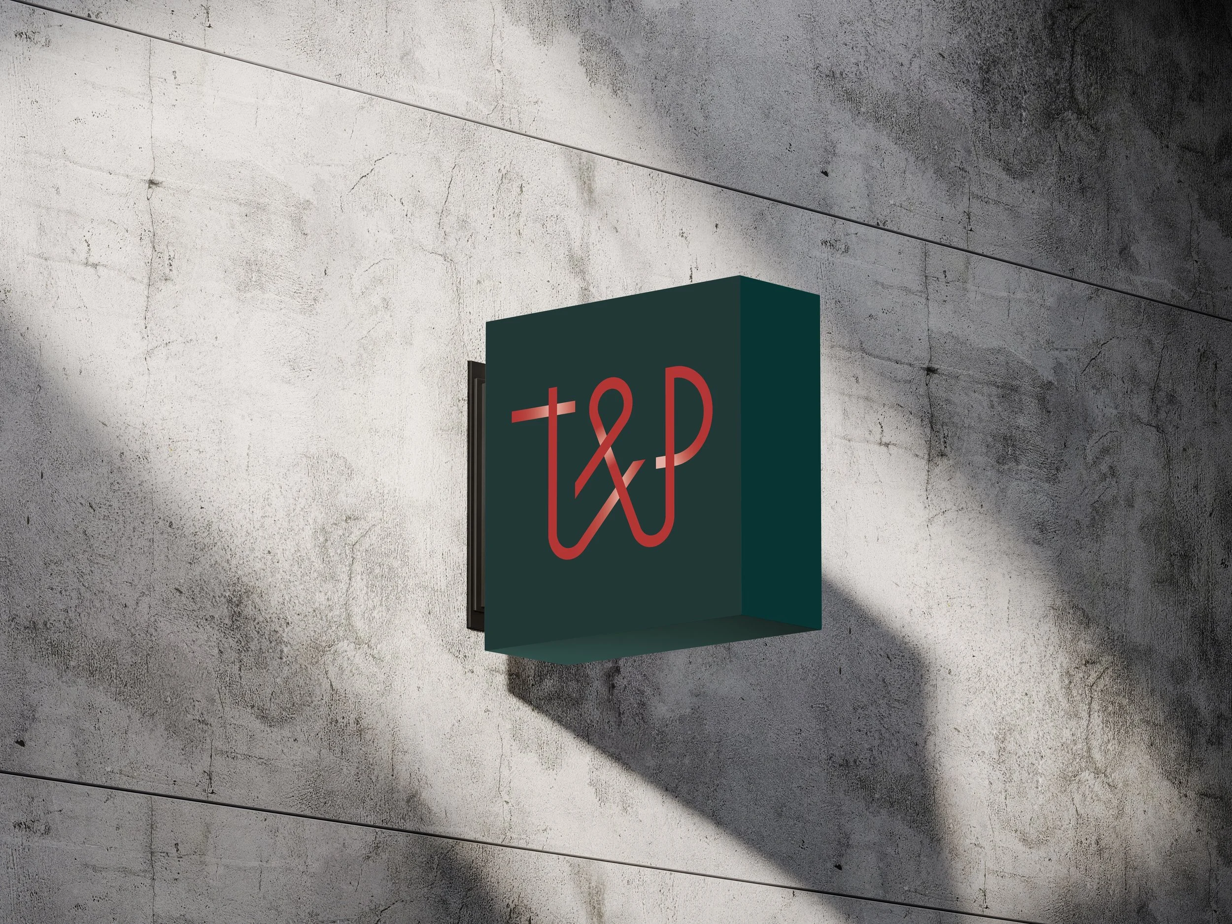 Un panneau lumineux avec le logo de T&P, fixé à un mur en béton gris.