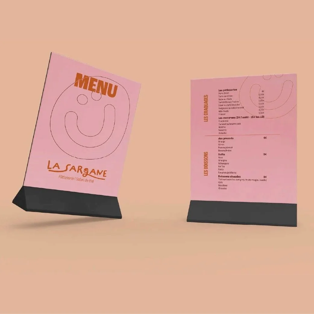 Deux menus de pâtisserie rose avec un design simple et un sourire dessiné, placés sur une surface beige