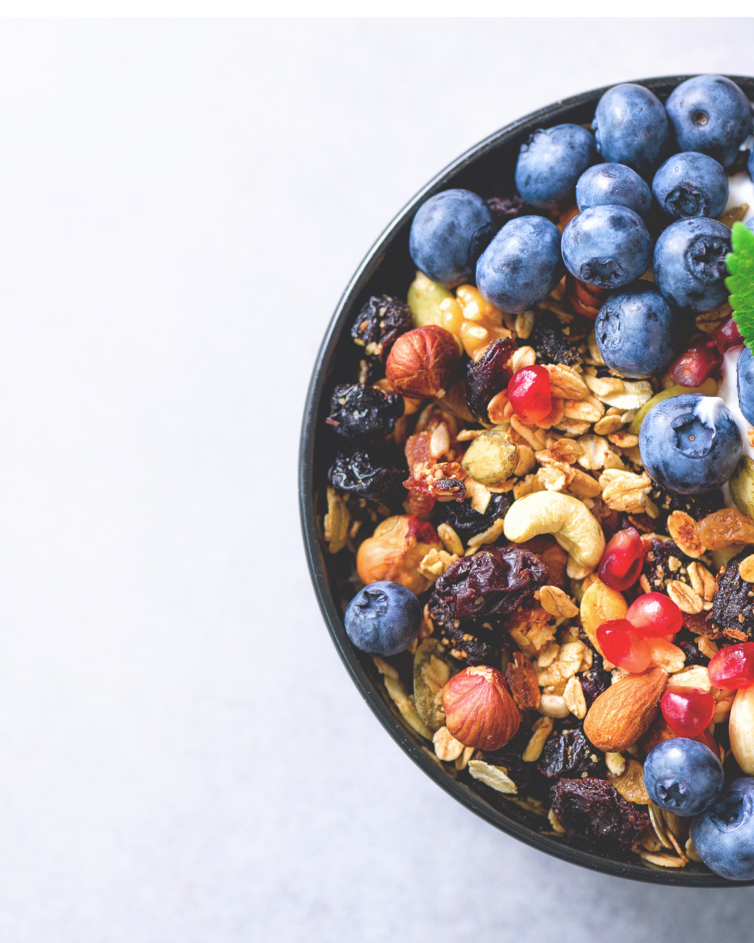 Close-up of a bowl of granola topped with blueberries and other dried fruits and nuts on a white background.