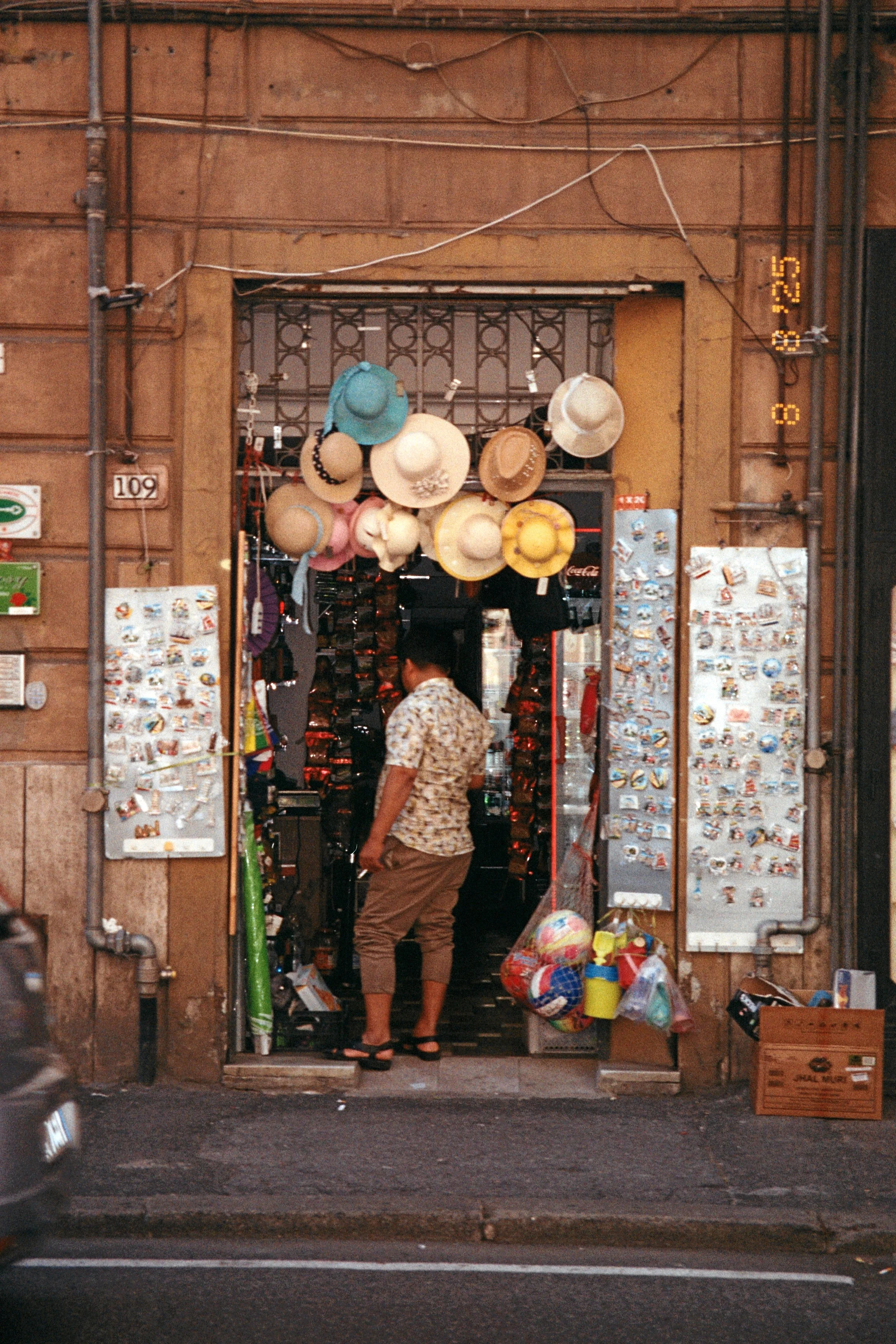 A small street shop with hats hanging above the entrance and various souvenirs and magnets on display outside.