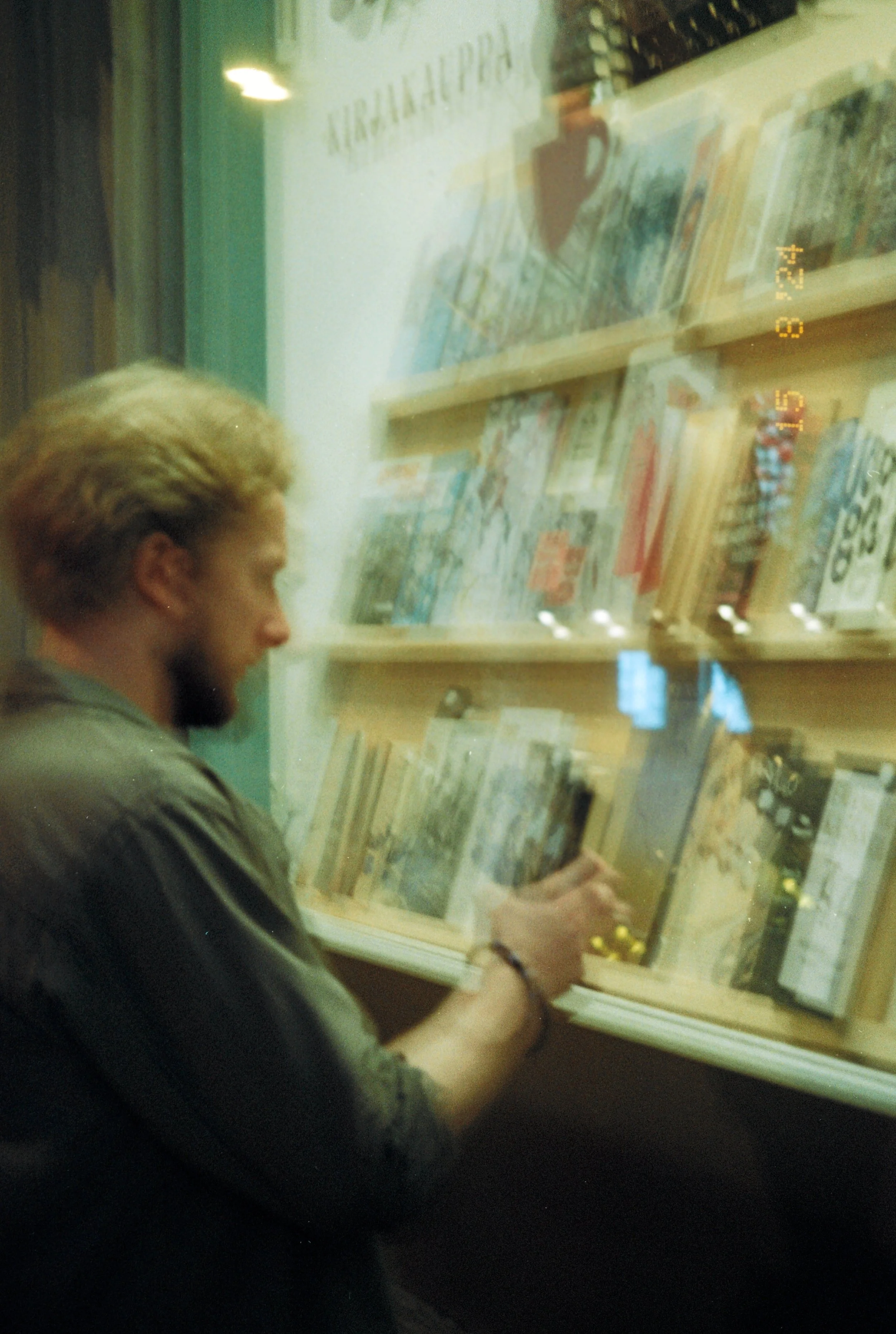 A man with blonde hair browsing books through a window display at a bookstore on a city street.
