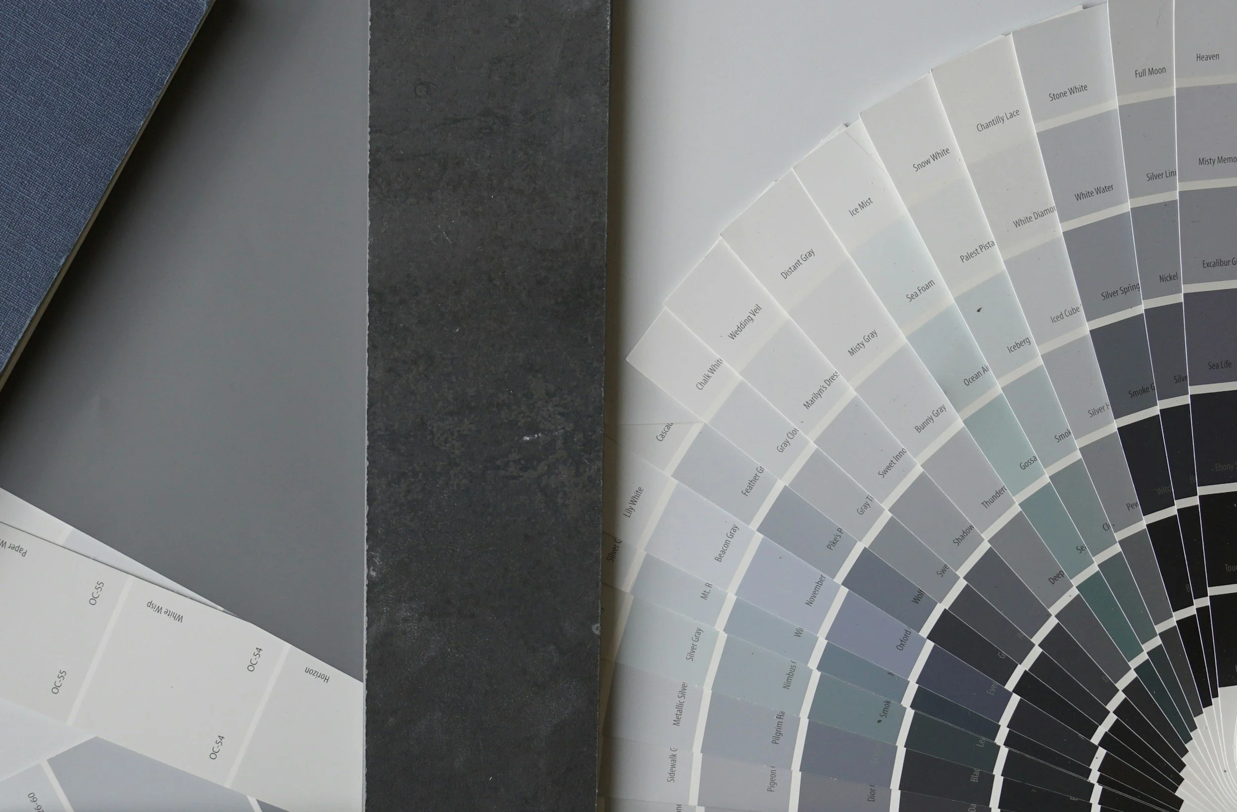 Tarjetas de muestras de colores en tonos grises, blancos y neutros, formando un abanico, con una superficie negra y otra gris como fondo.