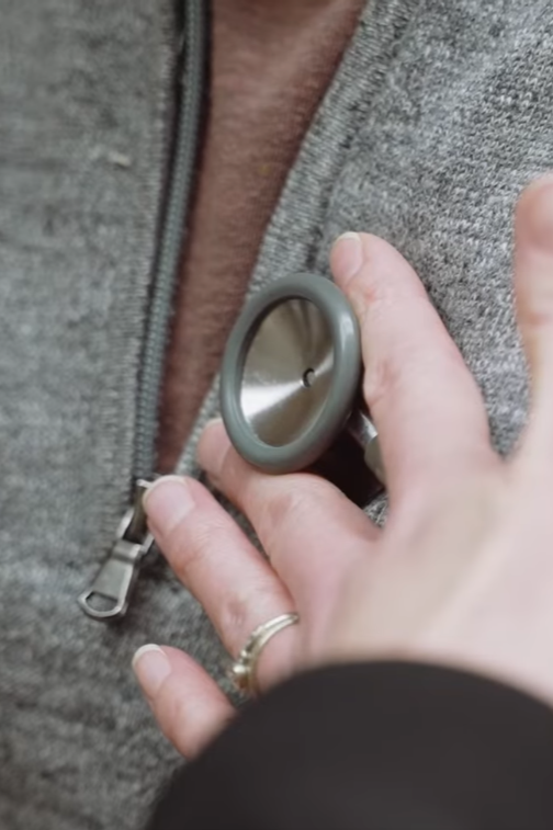 Person with a gray button on a gray jacket holding a blood glucose meter.