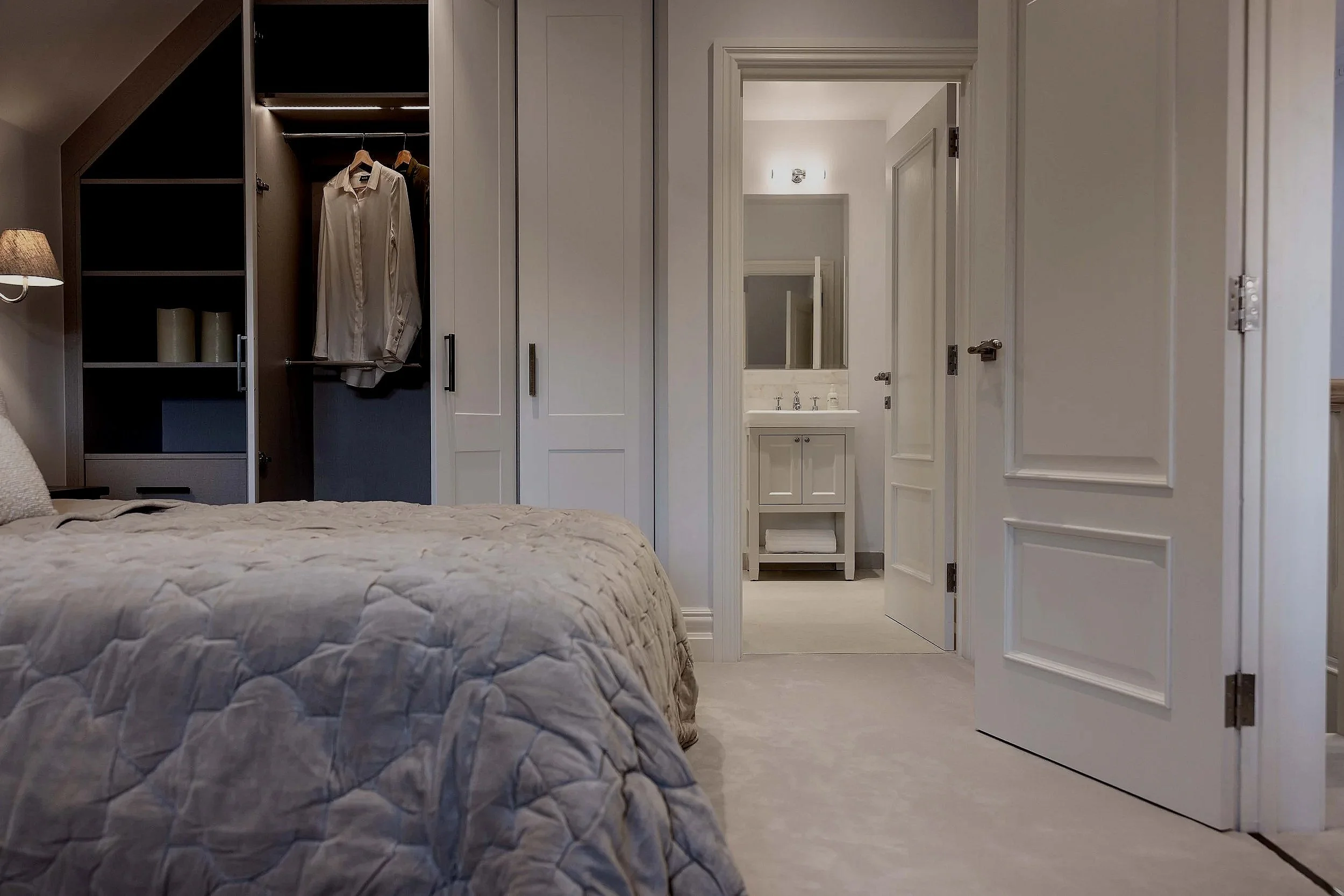 Bedroom with bed, open closet with hanging clothes, and a bathroom vanity with mirror