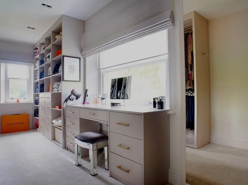 Organized bedroom area with shelves, a desk with a mirror and chair, and open closet with hanging clothes.
