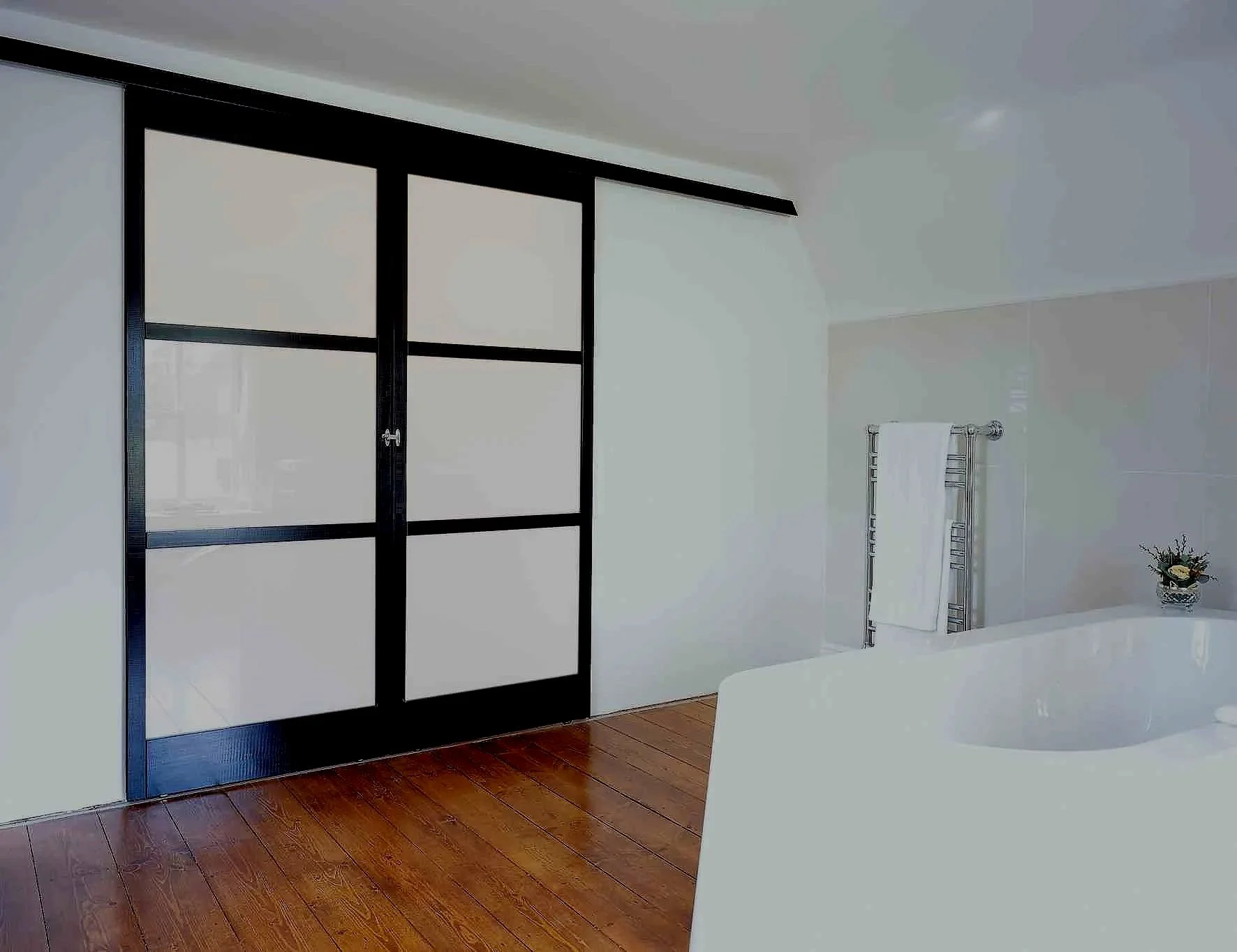 Modern bathroom with wooden floor, black sliding door, towel rack with white towel, and a small potted plant on a ledge.