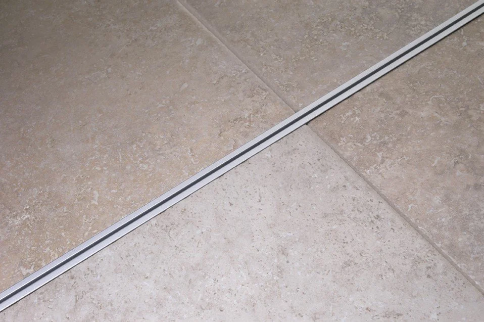Close-up of ceramic floor tiles separated by a metal strip, likely part of a shower or bathroom.