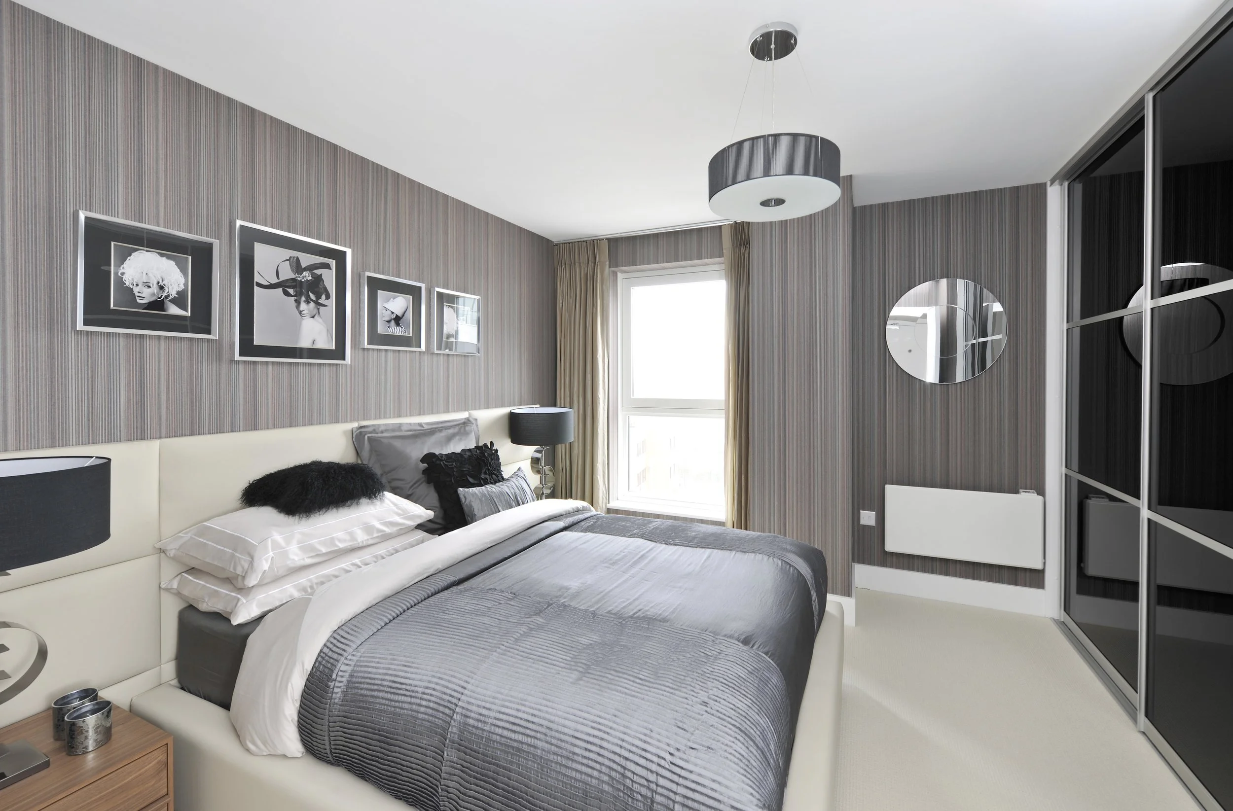 A modern bedroom with a bed, black and white framed art, lamps, mirror, and mirrored closet doors.