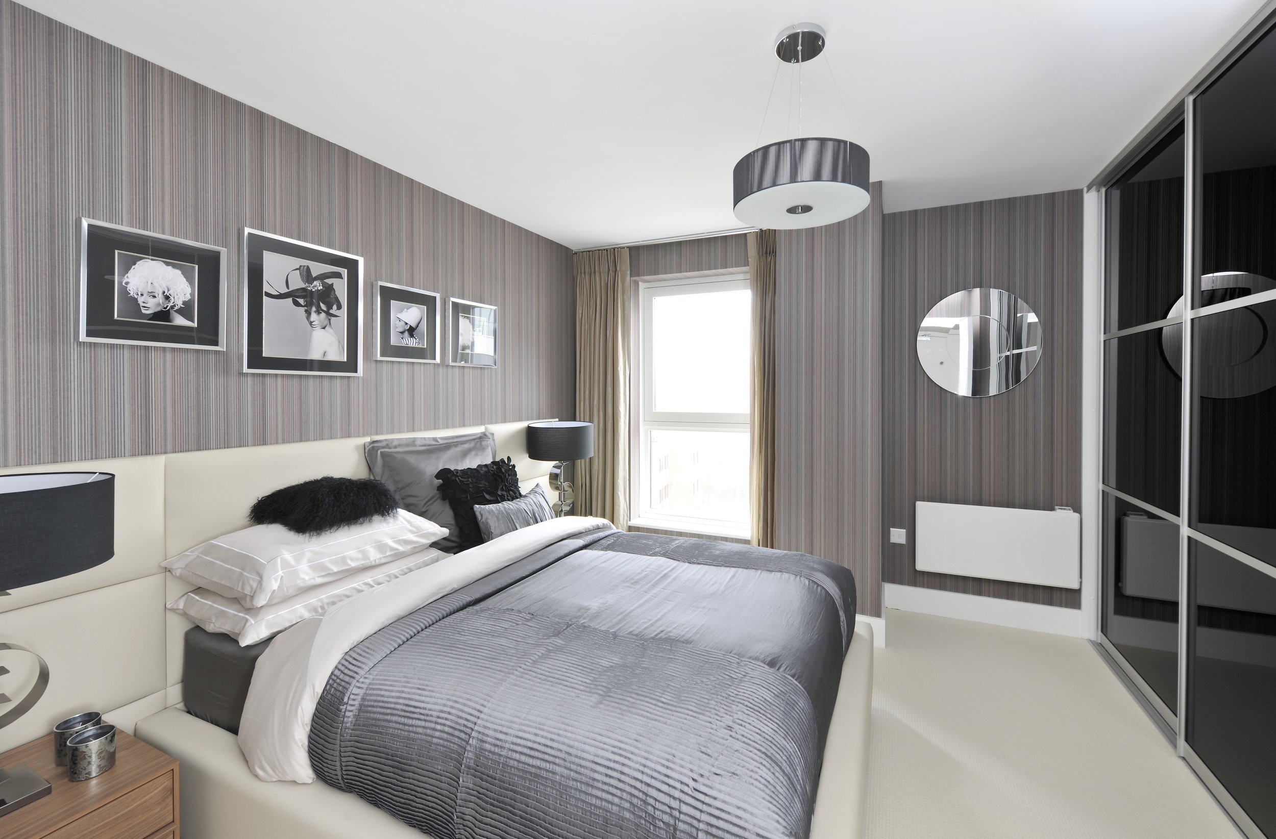 A modern bedroom with a bed, black and white framed art, lamps, mirror, and mirrored closet doors.