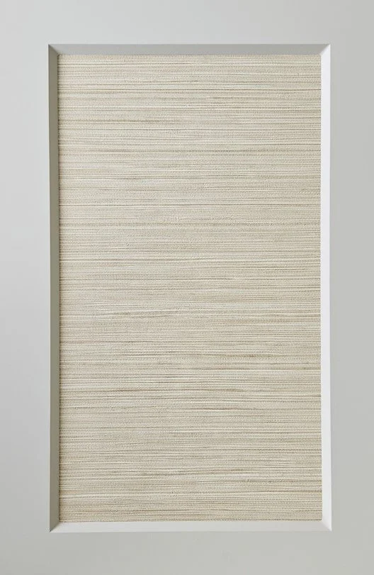 A rectangular white door with a fabric-covered panel in the center, framed by a white border, against a light gray wall.