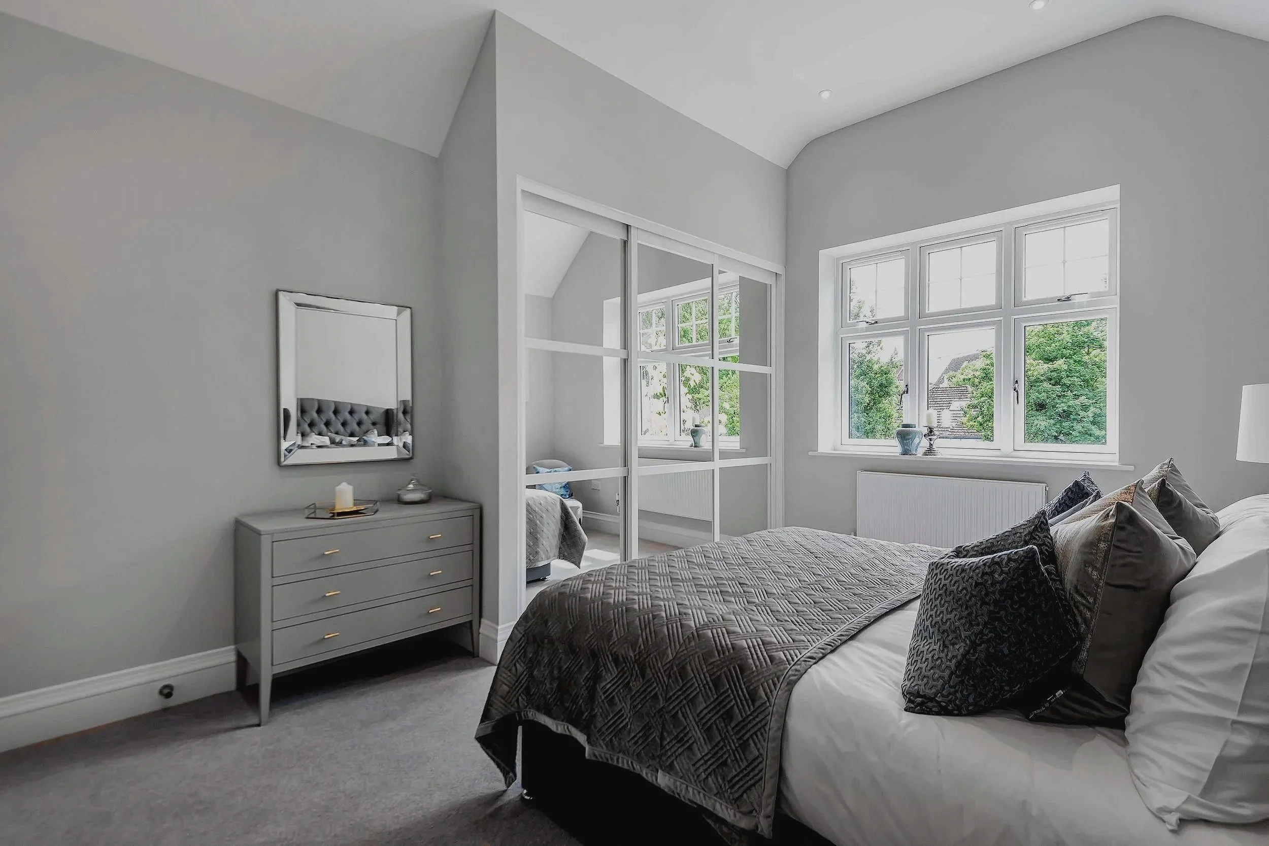 Bright, modern bedroom with large window, gray walls, and a bed with gray and black pillows.
