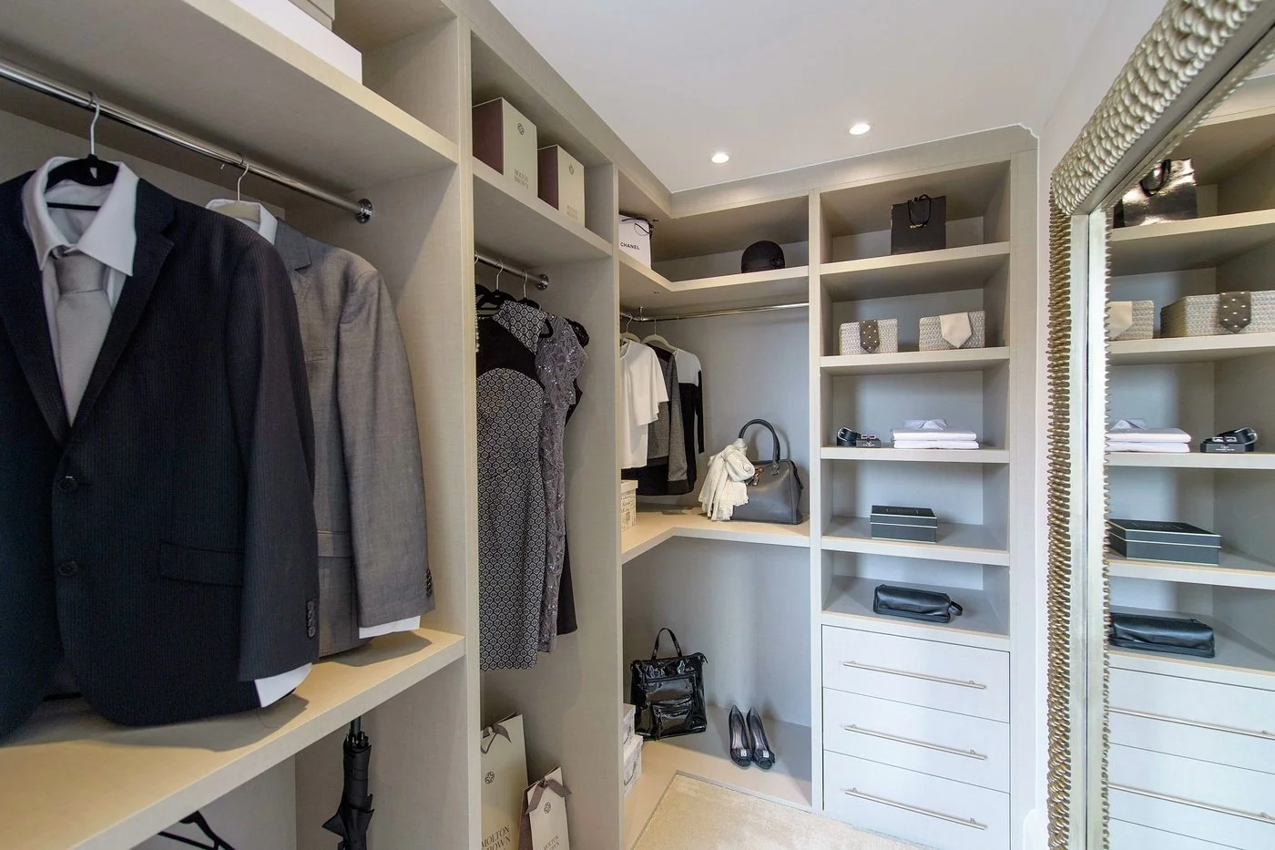 Well-organized walk-in closet with suits, dresses, handbags, shoes, and boxes on shelves.