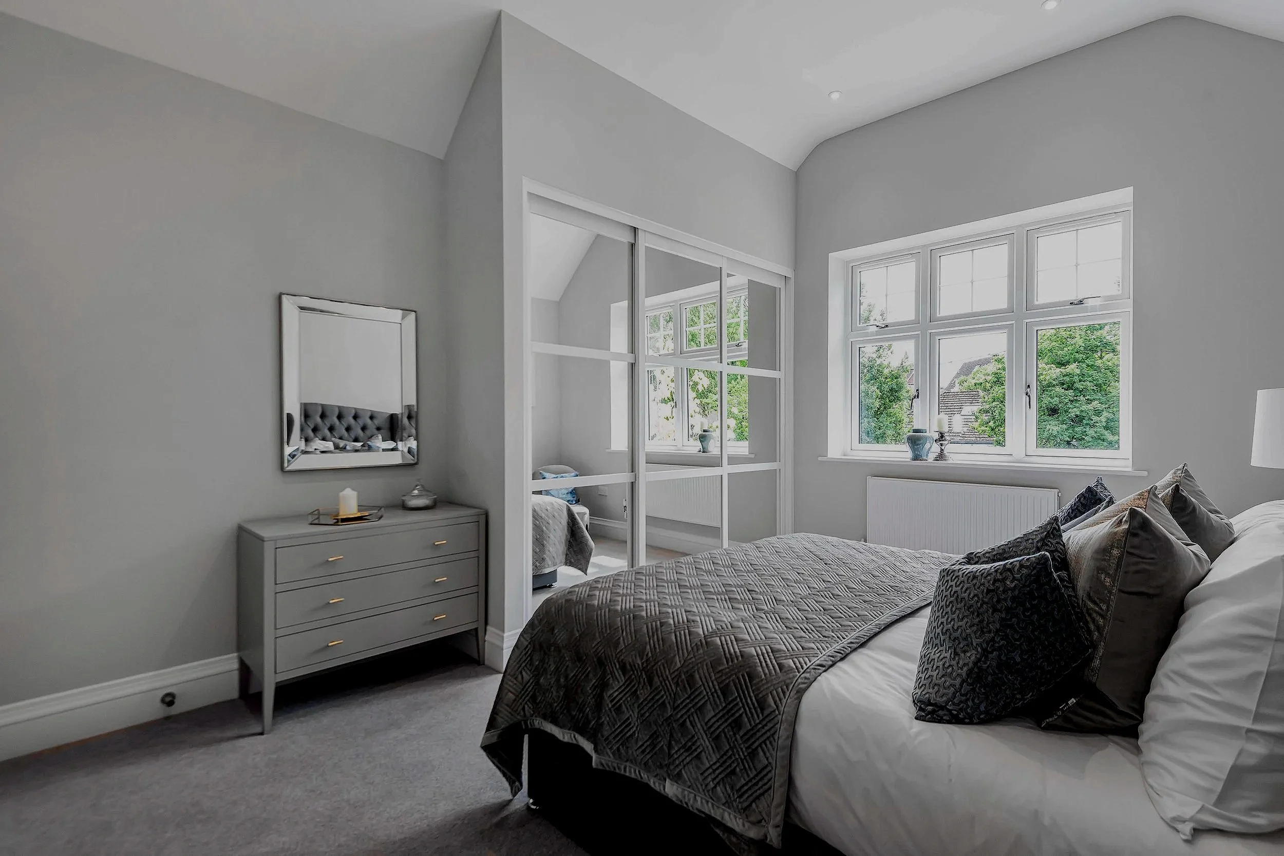 Modern bedroom with large window, gray furniture, and sitting area separated by glass partition