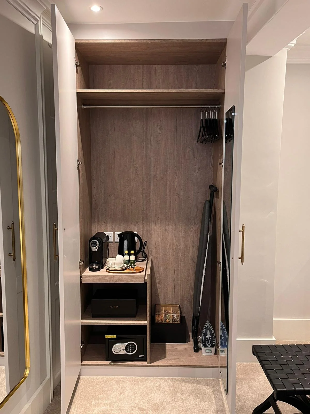 Empty hotel closet with some amenities, two irons, a safe, coffee maker, cups, and bottled water.