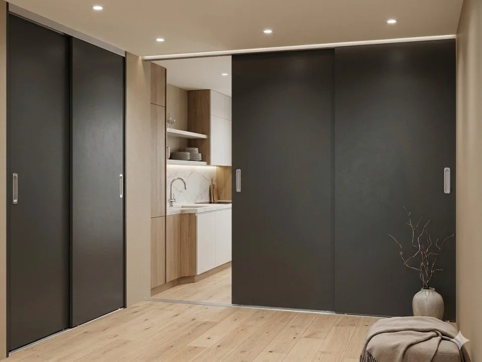 View of a modern kitchen with a sliding door separating it from a living area. The kitchen has wooden cabinets, open shelving, and white lower cabinets. The living area features light wooden flooring, a large vase with branches, and a piece of fabric or blanket on furniture.