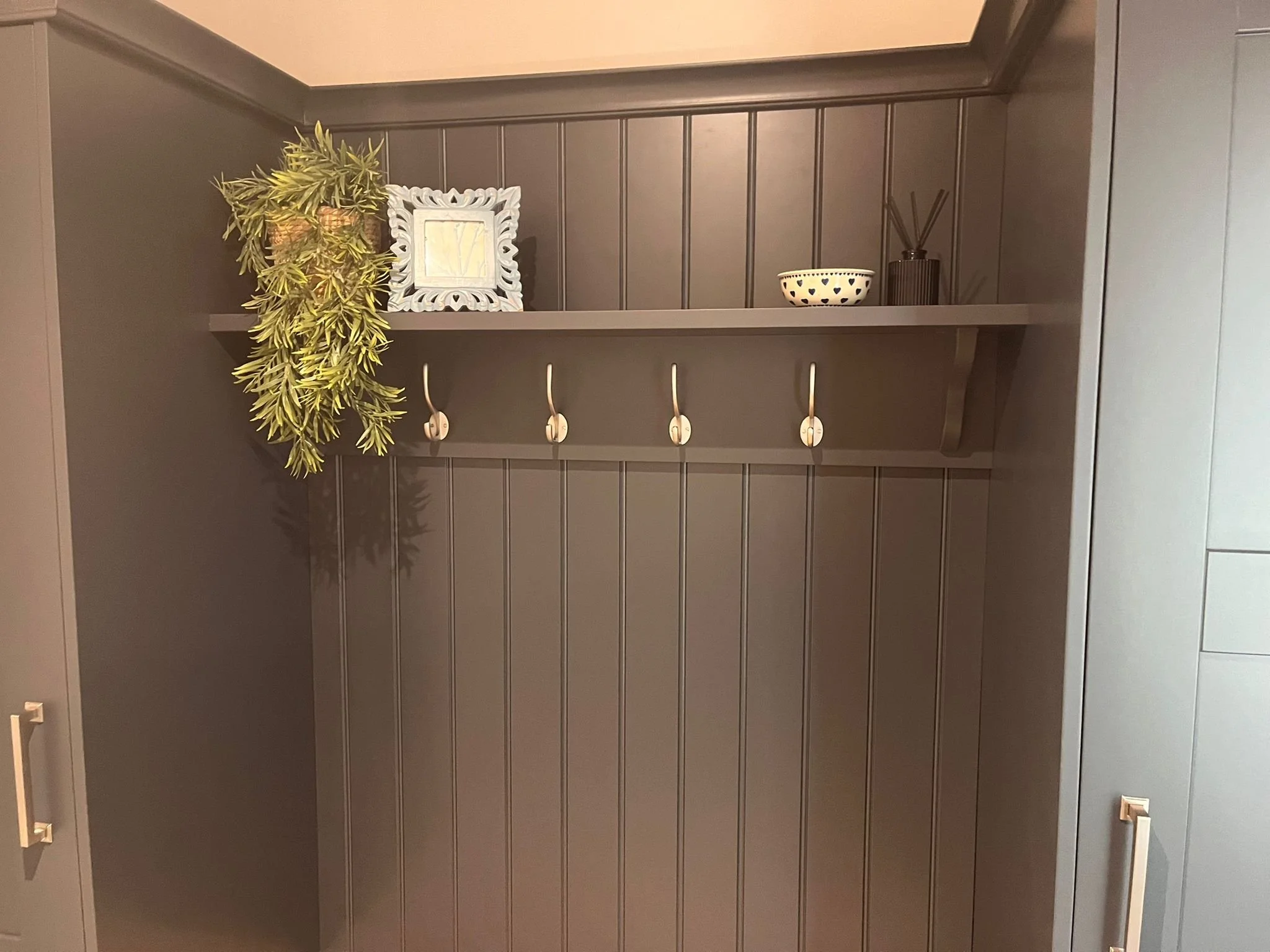 Gray wall with a wooden shelf holding decorative items and hooks, with a plant hanging off the shelf.