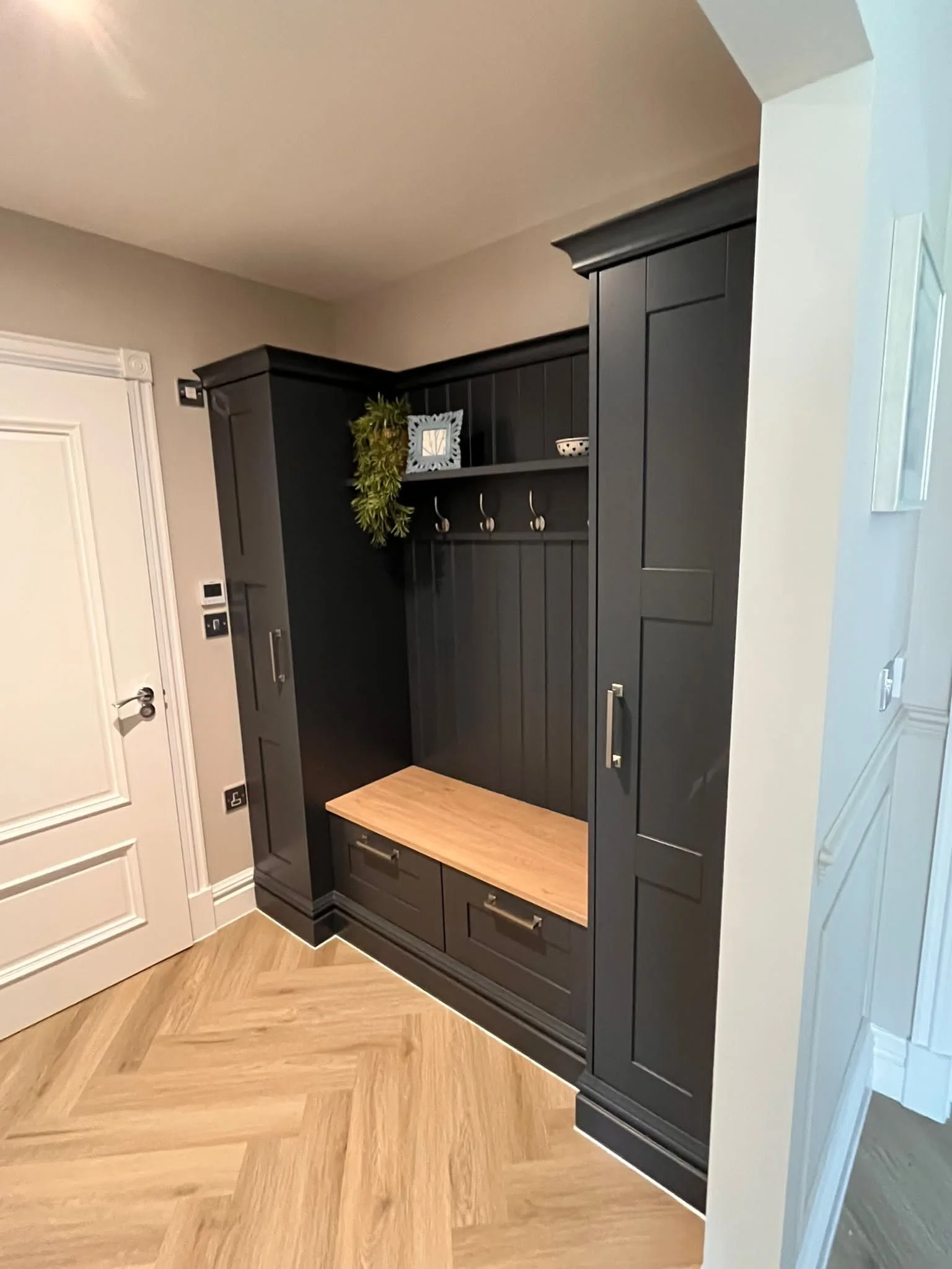 Black wooden entryway bench with hooks, shelves, and drawers in a home interior.