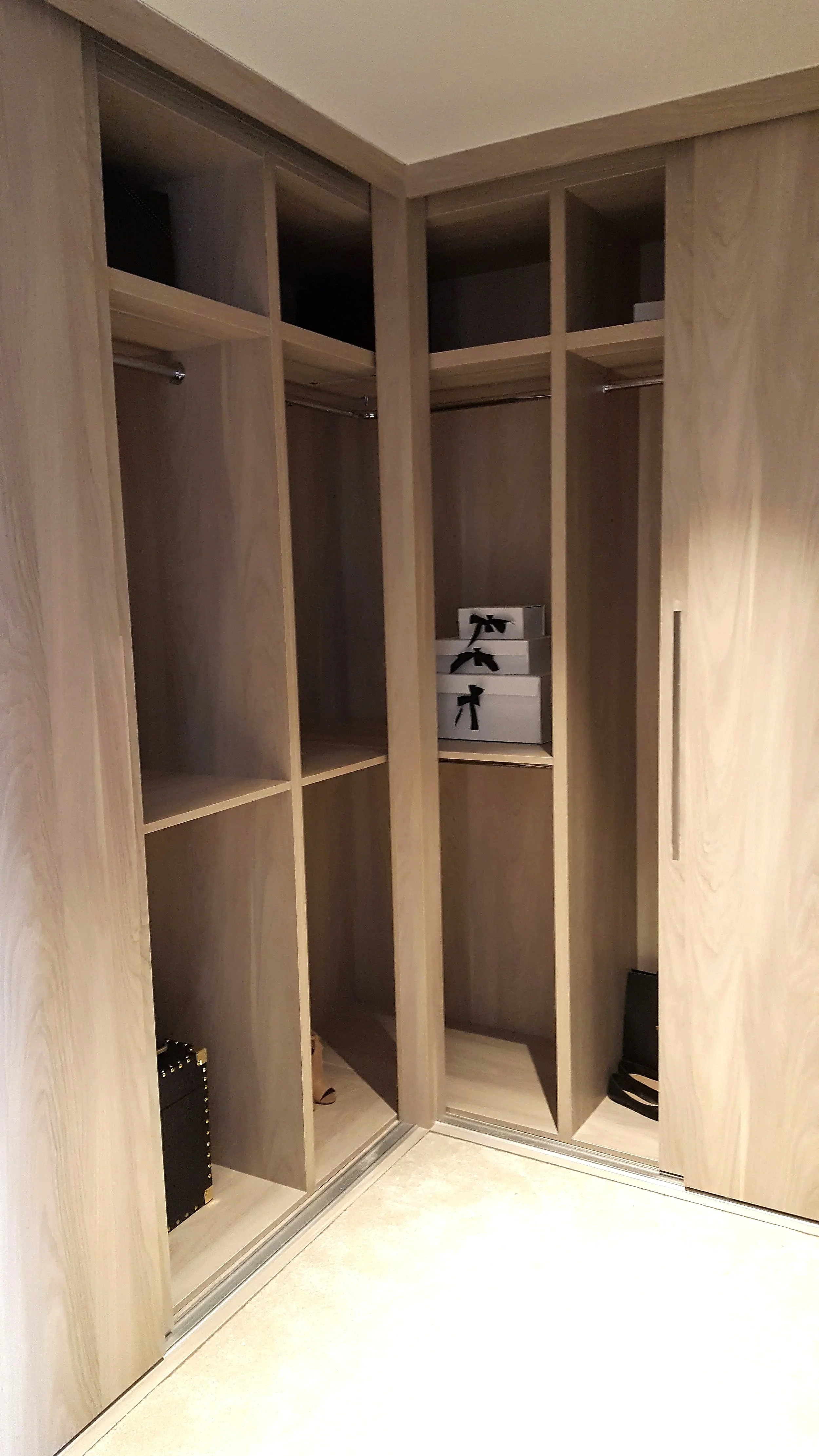 Empty wooden closet with glass sliding doors, some boxes on the middle shelf, and some items on lower shelves.