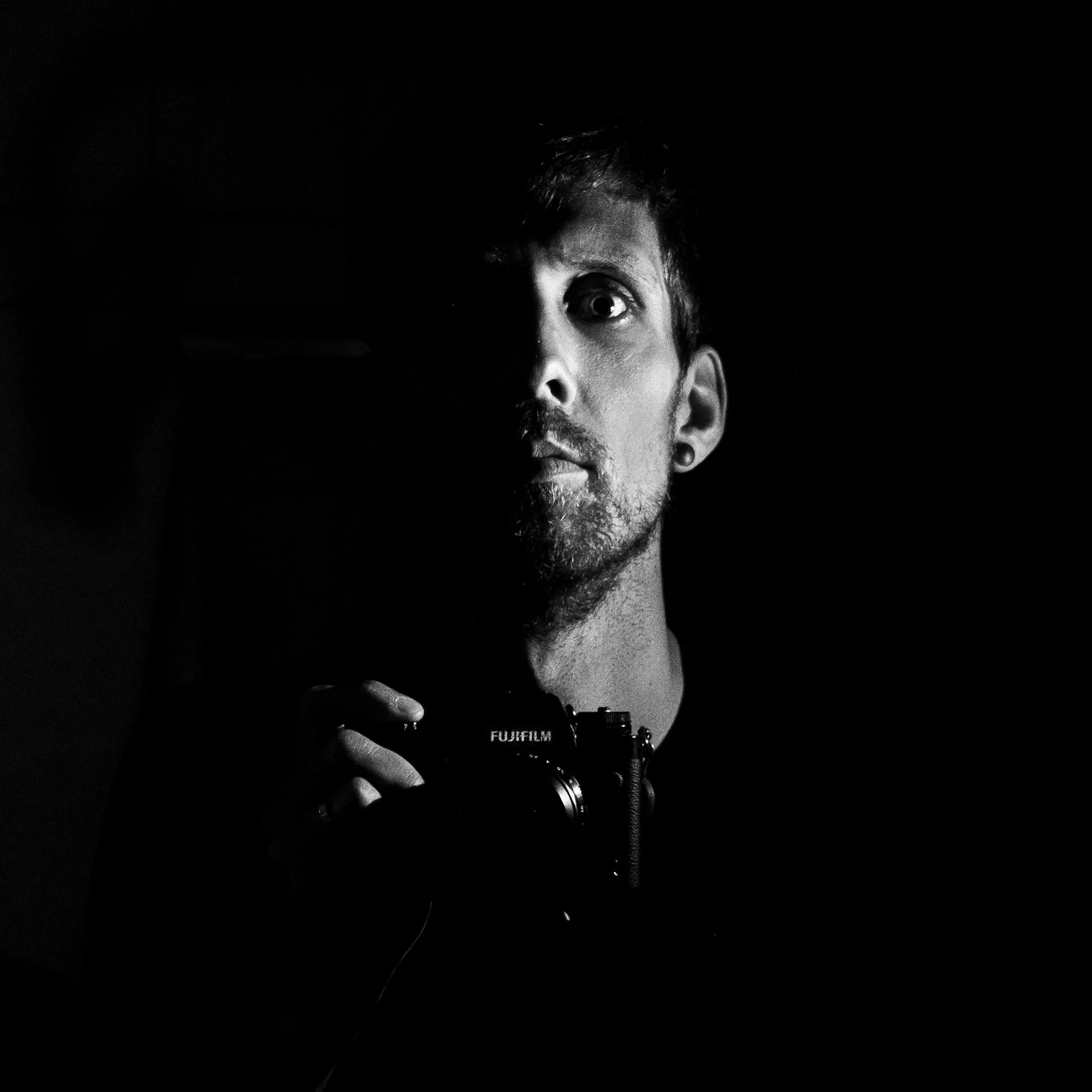 Schwarz-Weiß-Foto eines Mannes, der eine Kamera hält, halb im Schatten, mit einem ernsthaften Gesichtsausdruck.