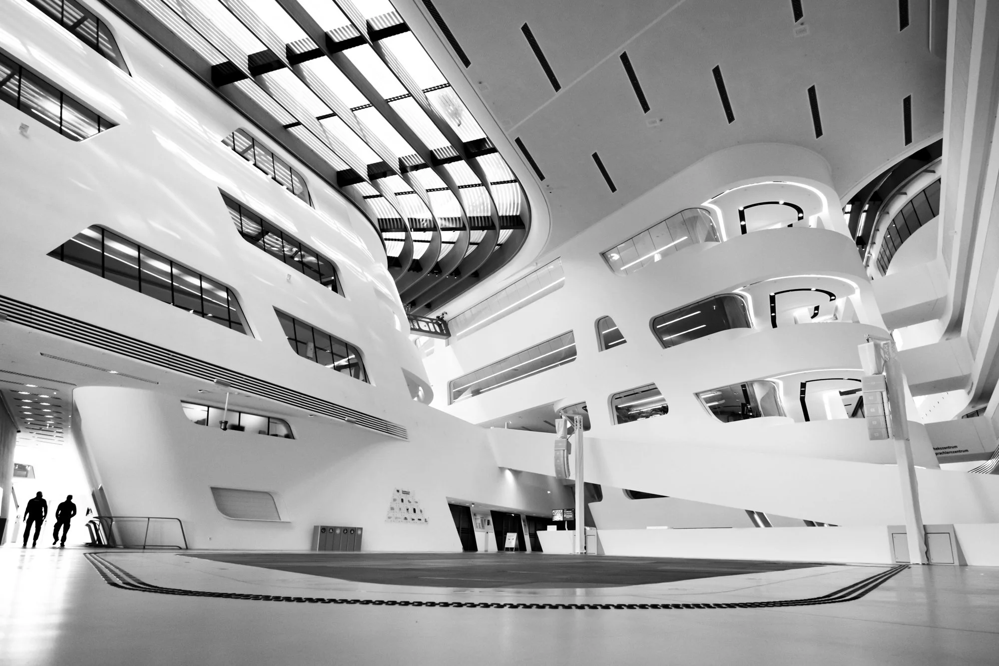 Modernes, futuristisches Architekturgebäude mit weißen, geschwungenen Linien und mehreren Etagen, innen mit glatten Flächen und großen Fenstern, im Schwarz-Weiß-Format.