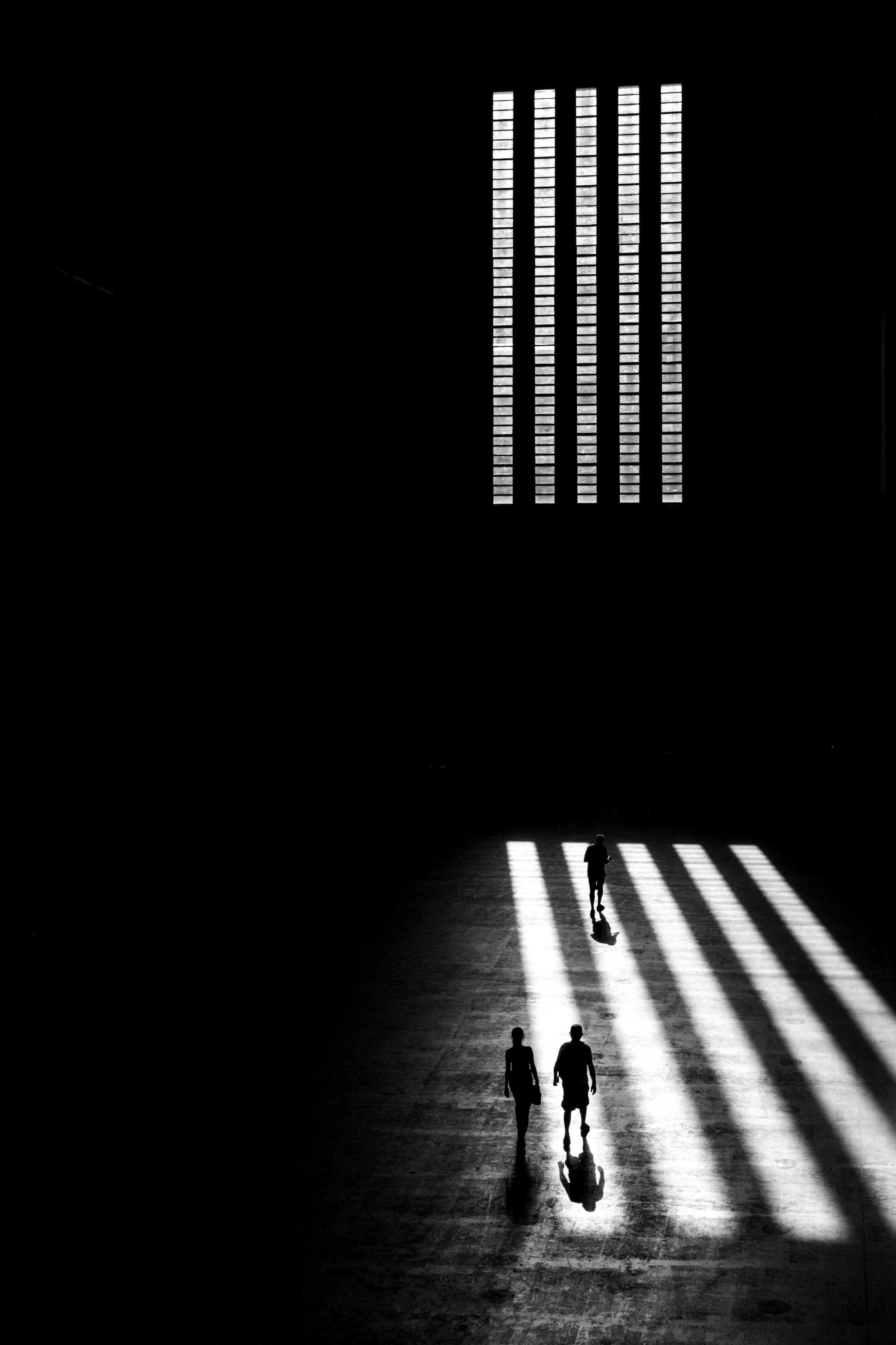 Drei Personen laufen durch einen dunklen Raum, er leuchtet nur durch Lichtstrahlen, die durch ein Fenster fallen, mit langen Schatten auf dem Boden.