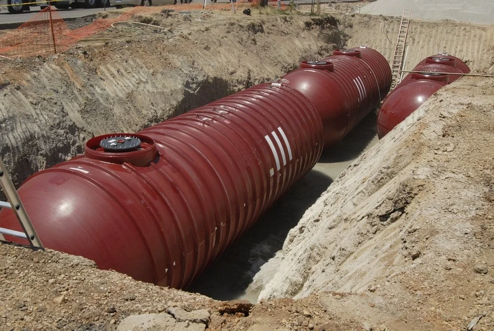 Large red underground storage tanks installed in a construction site excavated trench.