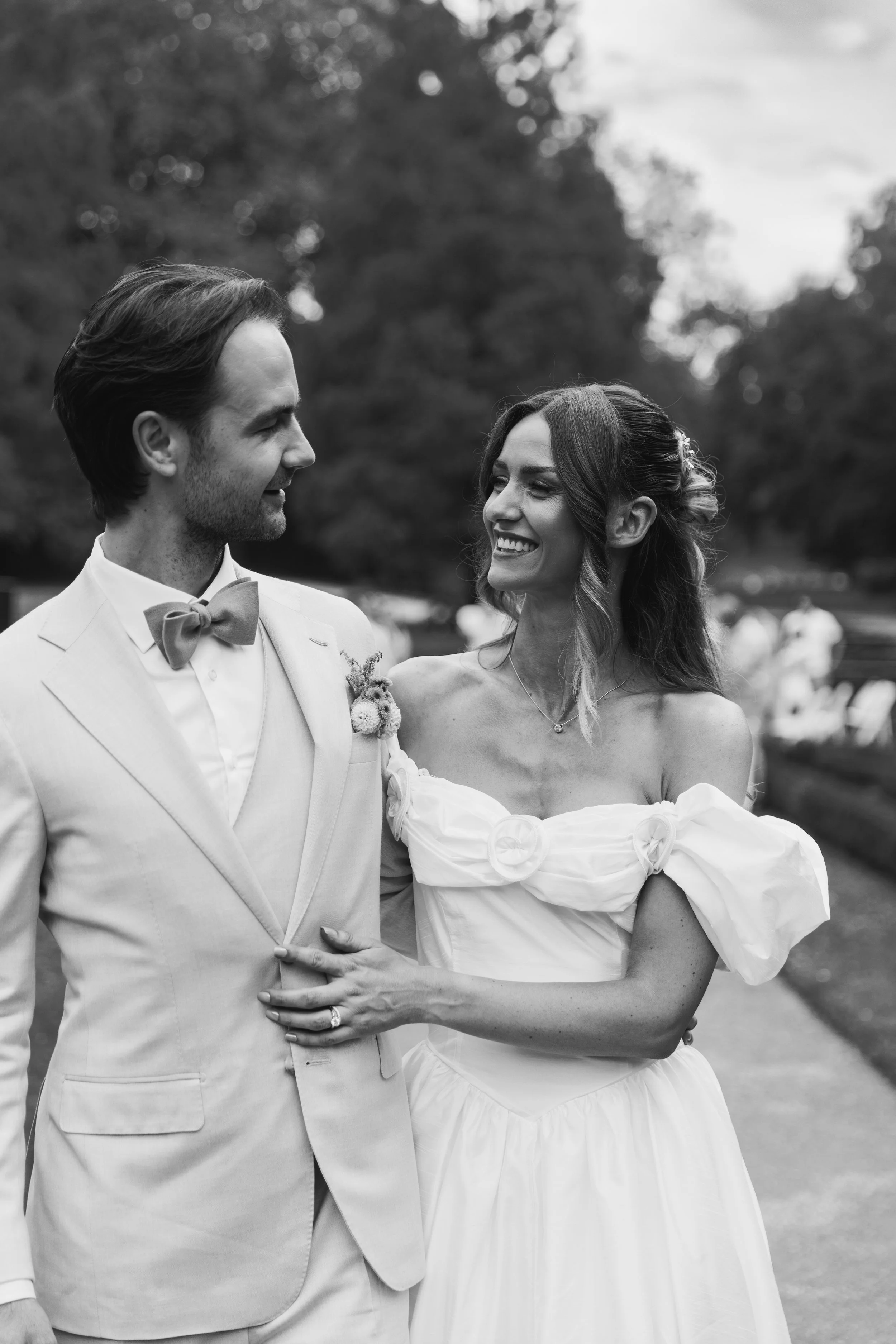 Black and white photo of a bride and groom standing close together, smiling at each other outdoors.