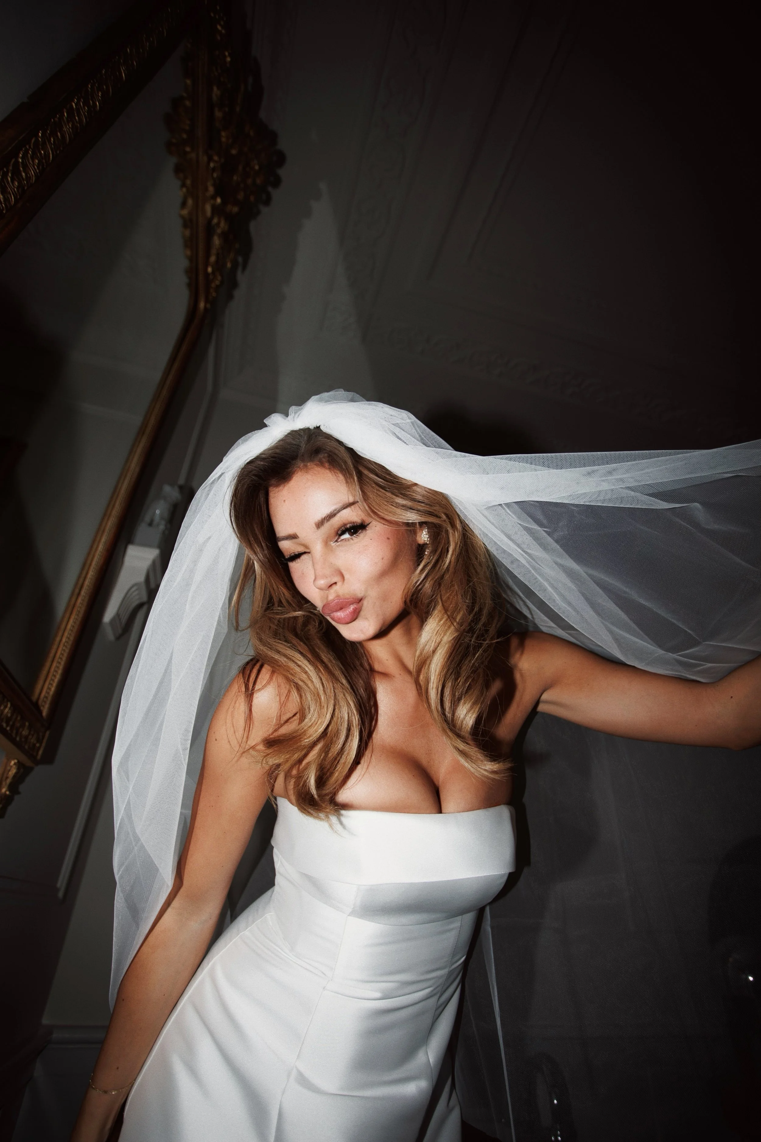 A woman in a white strapless wedding dress and veil making a kissy face at the camera.