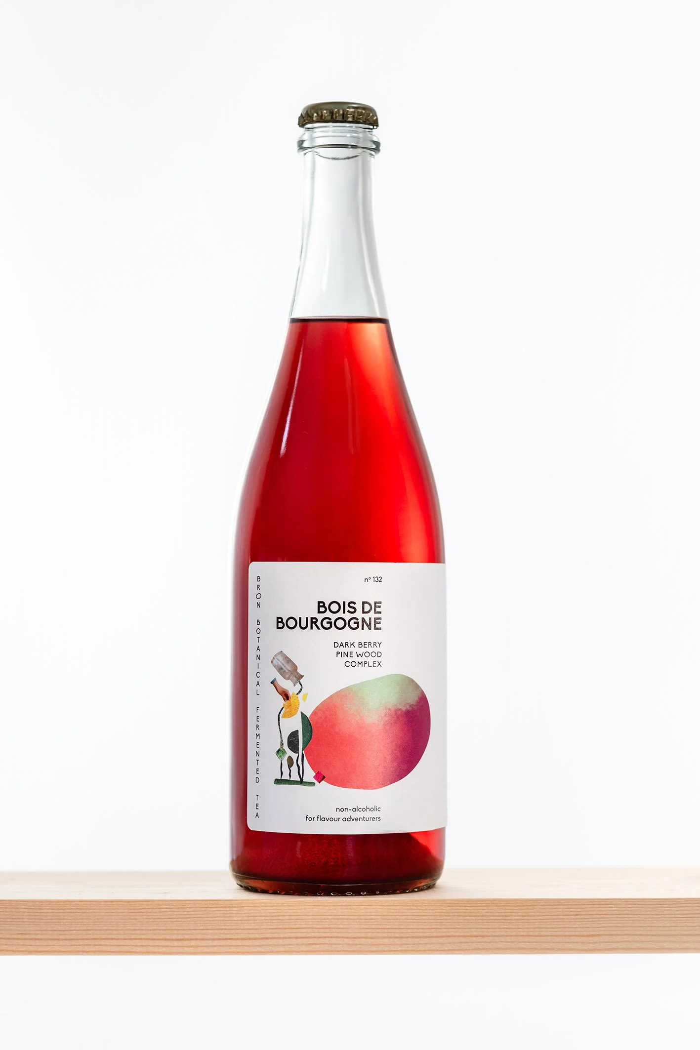 Flesje met een rood gekleurd drankje, label met rode illustratie, op houten vlak tegen witte achtergrond