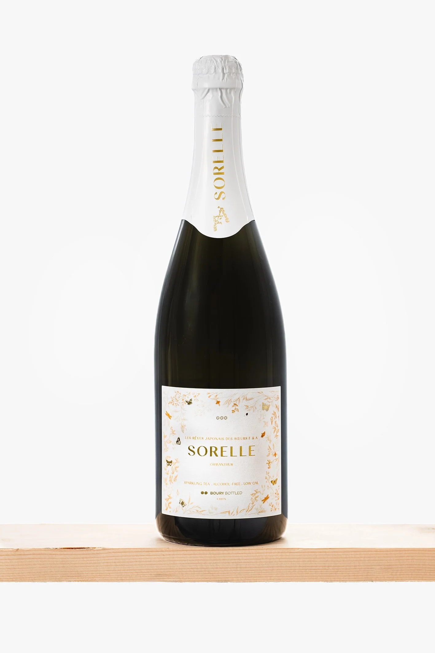 Fles wijn met witte en gouden label en witte capsule op een houten plank.