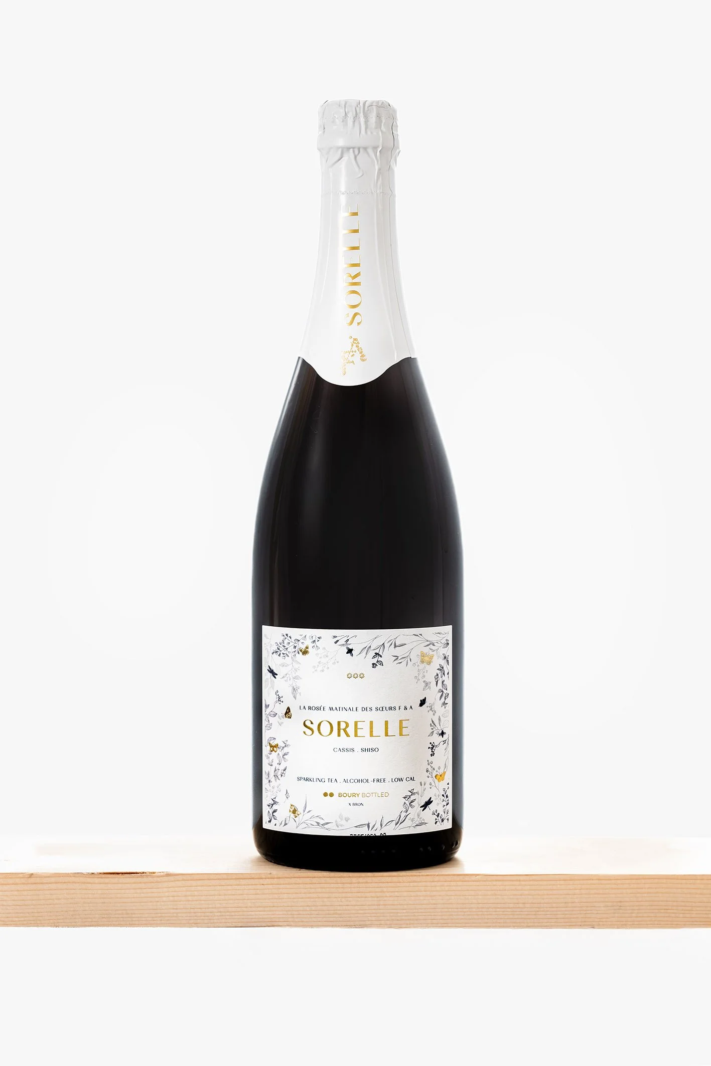 Flesje non-alcoholische sparkling thee met witte en goudkleurige label en witte folie op de dop, geplaatst op een houten plank.