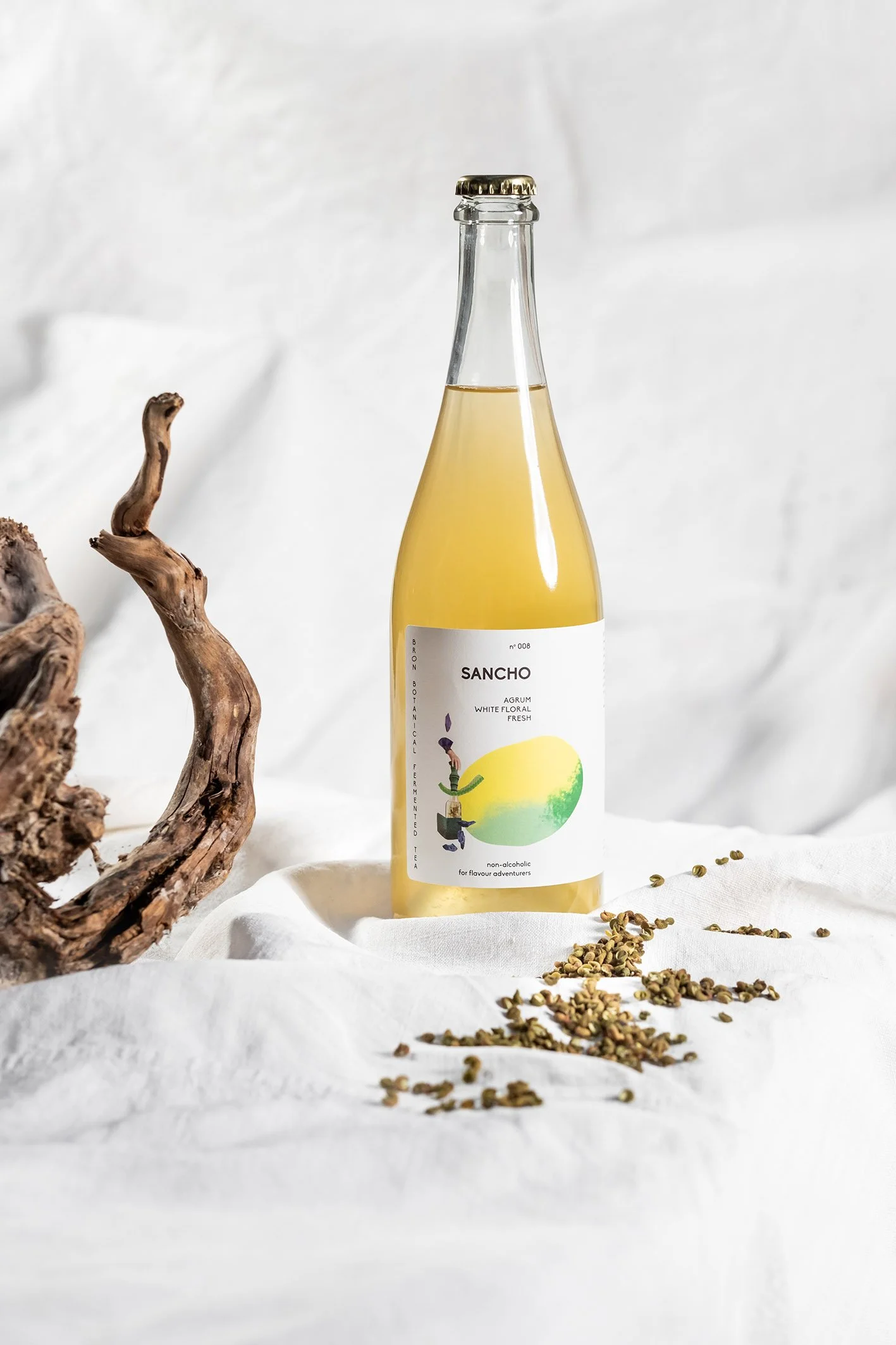 Flesje Sancho liefdevol gestyled met gedroogde kruiden en een stuk hout, op een witte doek met een witte achtergrond.