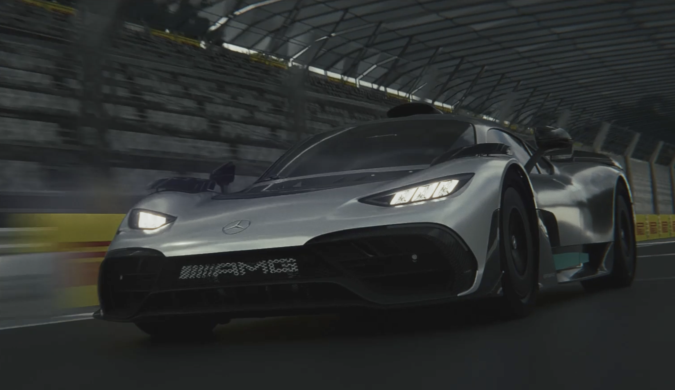 A silver AMG race car with the Mercedes-Benz logo on the front, speeding on a race track inside a covered stadium, with motion blur indicating high speed.