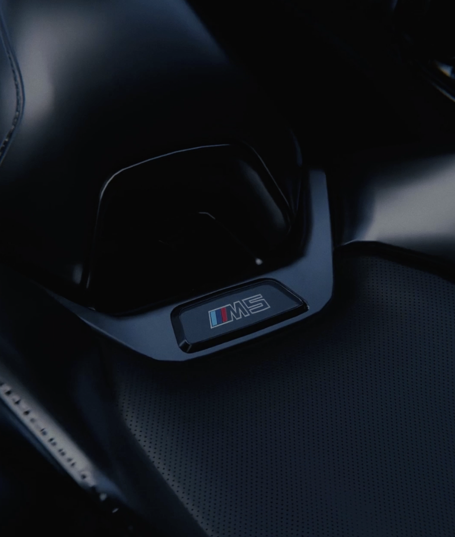 Close-up of the gear shift area inside a BMW M Series vehicle, featuring the M badge with red, blue, and light blue stripes.