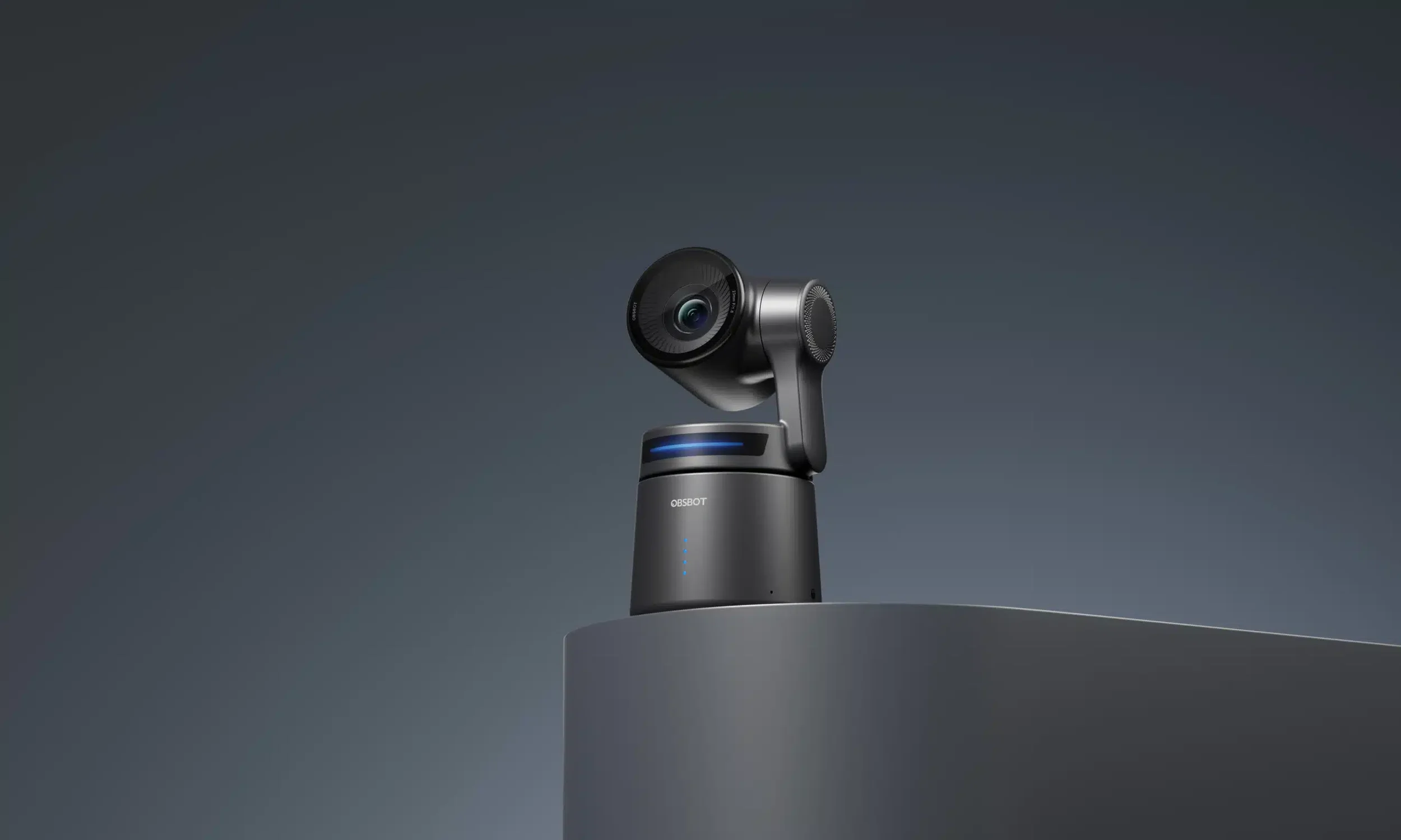 A sleek black 360-degree camera with a spherical lens mounted on a cylindrical stand, placed on top of a gray surface against a gradient gray background.