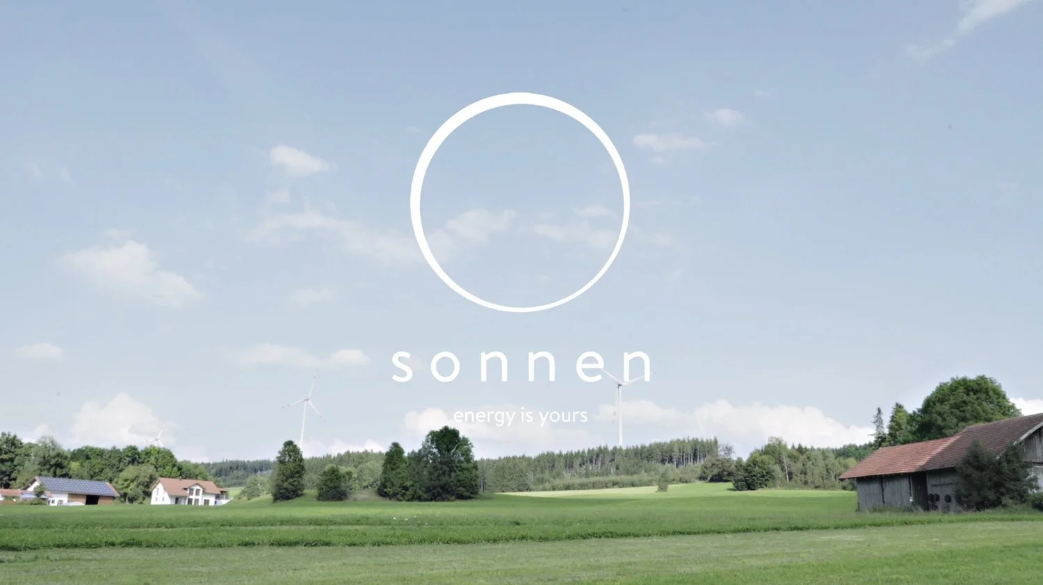 A landscape of green fields with a few houses and wind turbines under a partly cloudy sky, featuring a white logo with a circle and the word 'sonnen' and the phrase 'energy is yours'.