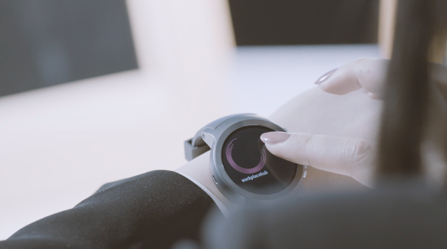 Close-up of a person wearing a smartwatch on their wrist, with their finger touching the screen that displays a circular progress indicator and the text 'workplacehub'.