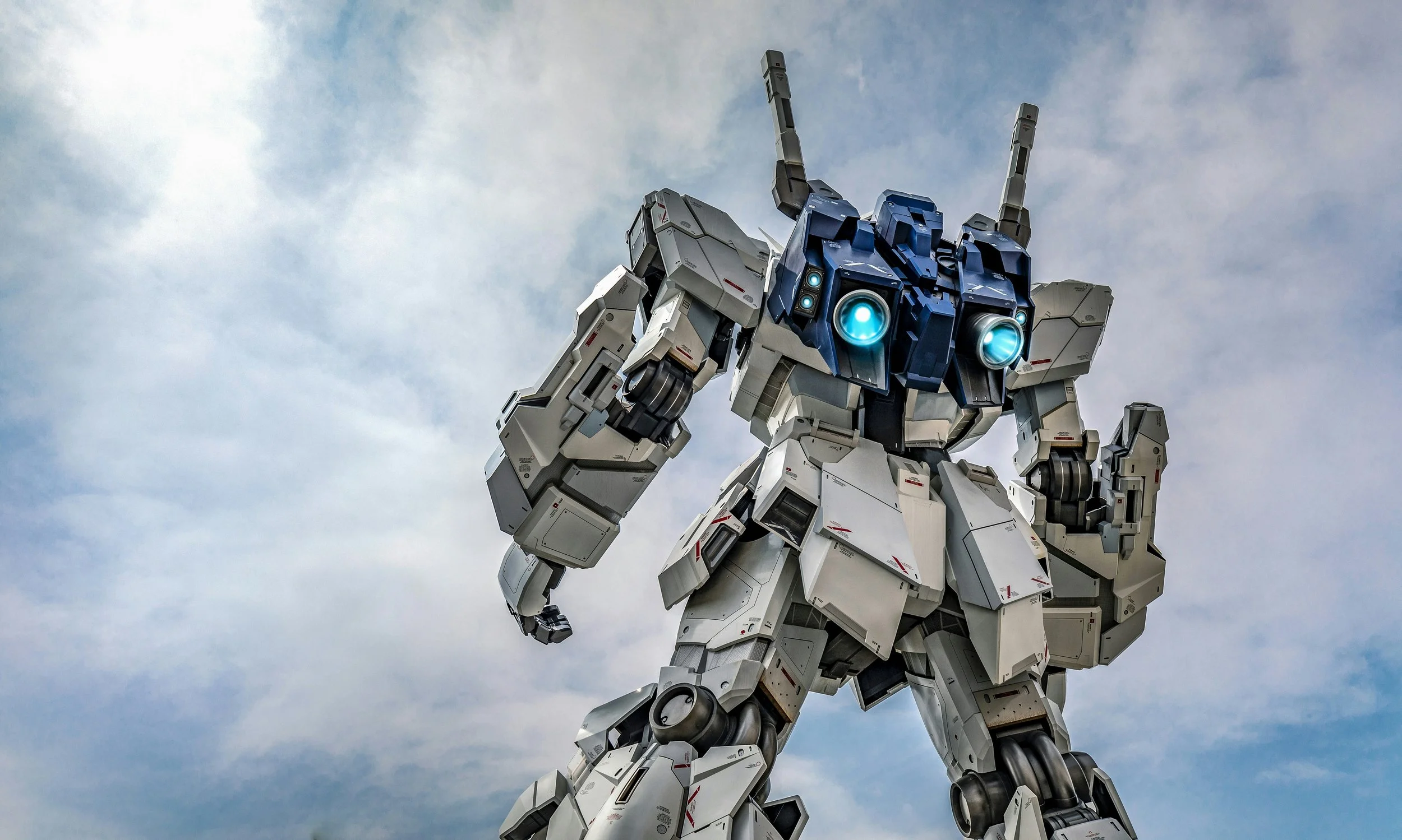A large transformer robot with glowing blue eyes standing against a partly cloudy sky.