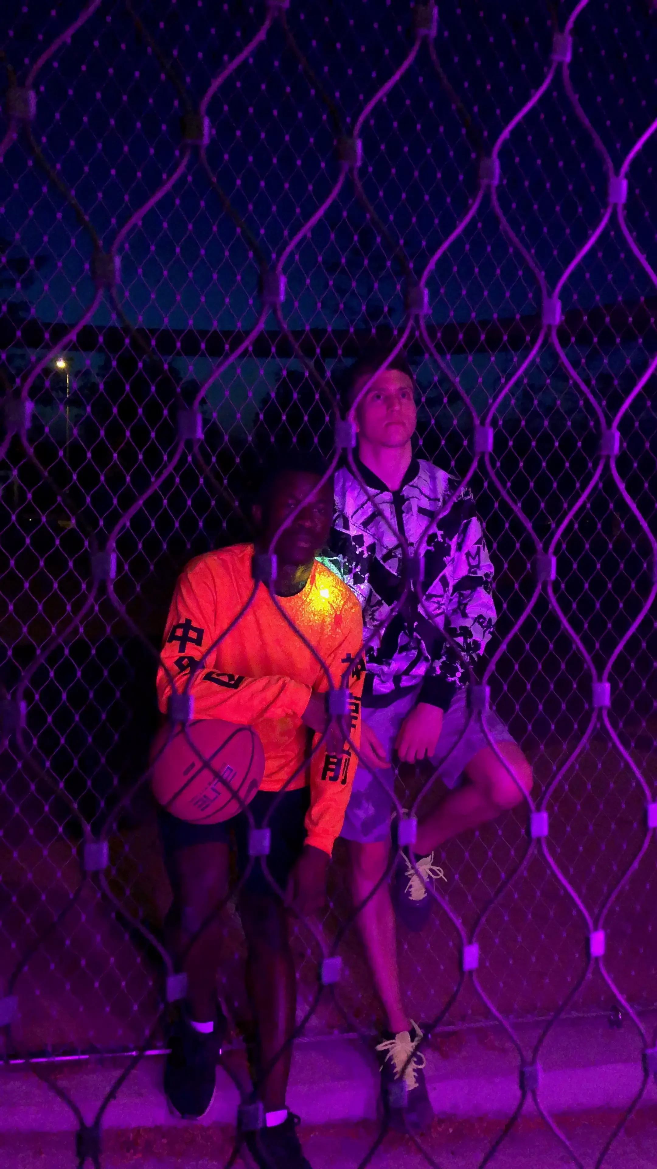 Kicks Social Media Spot: Stylische Neon-Beleuchtung in einem Streetwear-Werbespot mit zwei jungen Männern hinter einem Gitterzaun.