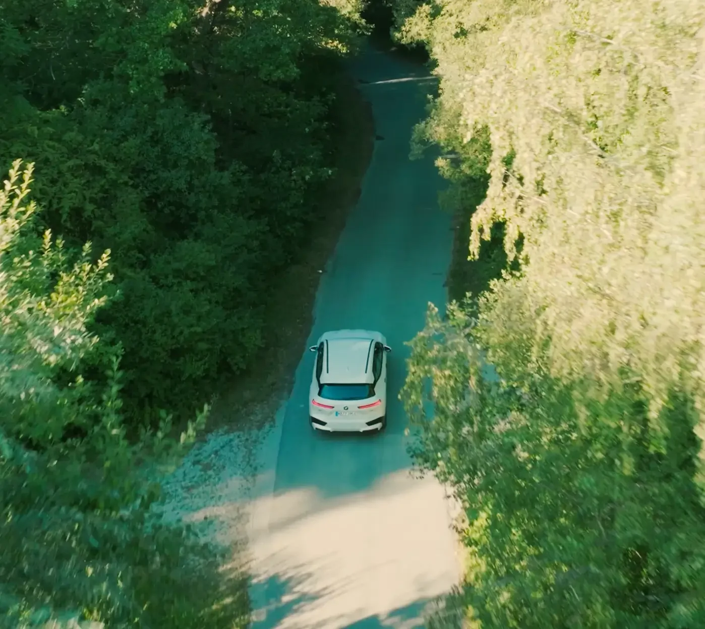 Designworks Agency Movie: Aerial-Drohnenaufnahme eines weißen Autos auf einer einsamen Straße mitten im tiefgrünen Wald.