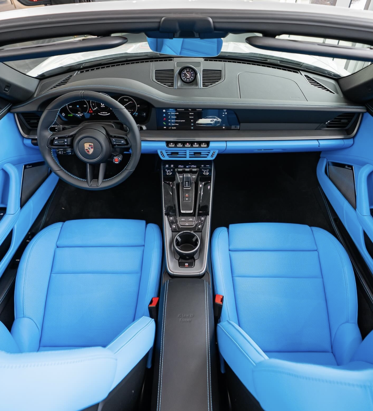 Interior of a modern Porsche car with bright blue seats, black dashboard, digital displays, and steering wheel.