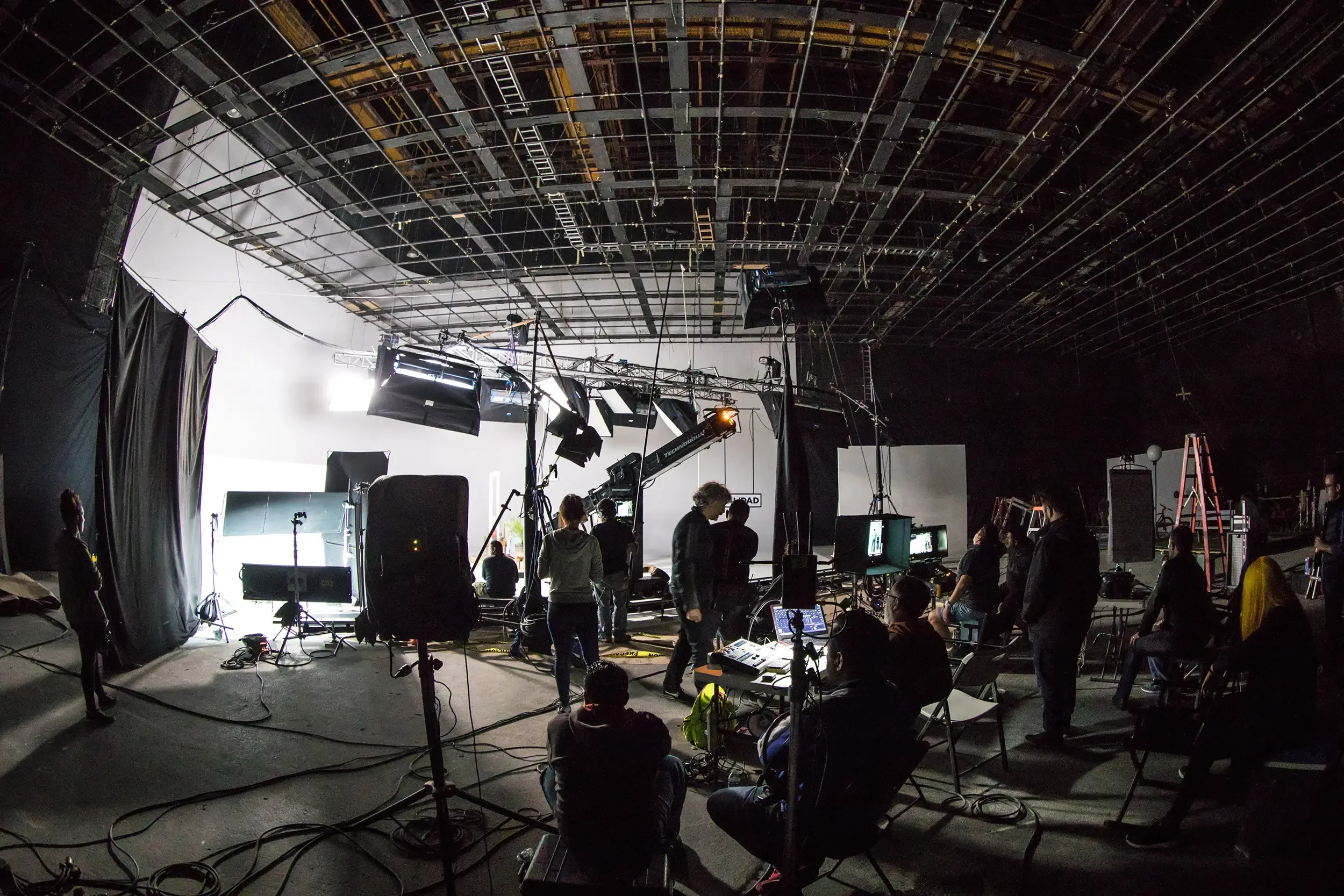 A Hollywood film studio set with crew members working, large lighting and camera equipment, and a green screen in the background.