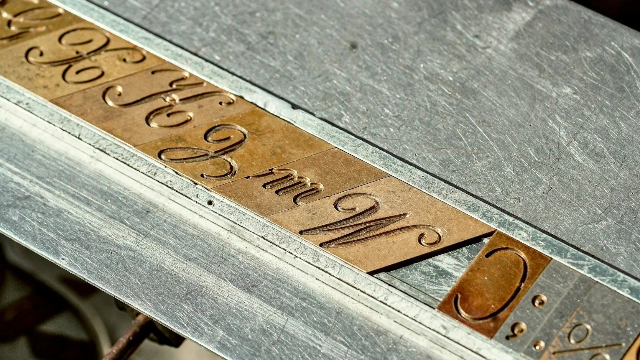 Close-up of metal stamps on a textured surface, spelling out words and numbers in a decorative font.