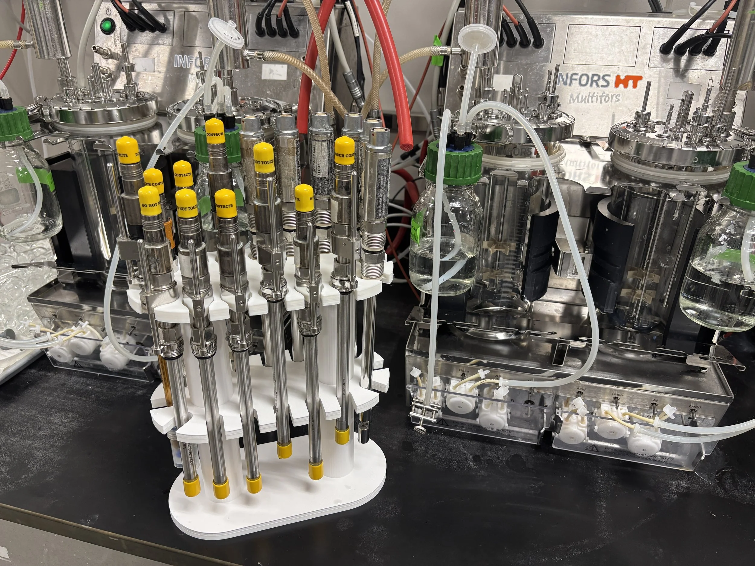 Laboratory equipment including multiple metal syringes, glass bottles with tubing, and a metallic machine with controls, used for scientific experiments or chemical processes.