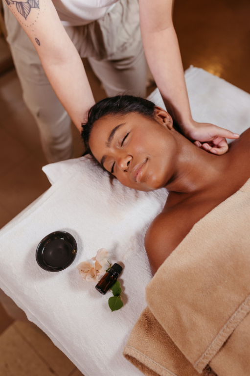 A woman receiving a massage in a spa, lying on her back with her eyes closed, a towel covering her lower body, and relaxing on a massage table.