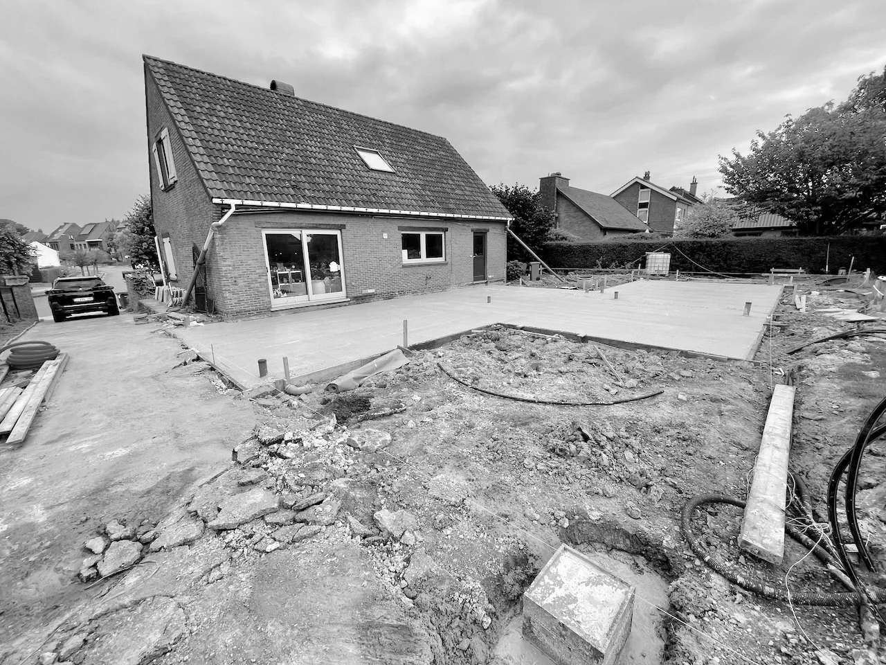 Tegels worden aangebracht op een oppervlakte voor een nieuw gebouw, rondom ligt bouwafval en bouwmaterialen, in een residentiële wijk met huizen en bomen op de achtergrond.