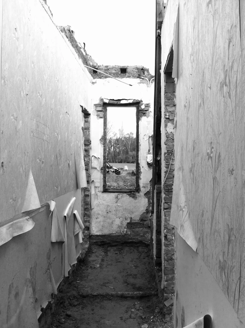 Een zwart-wit foto van een binnenmuur in een gebouw dat wordt gerenoveerd of onderconstructie is, met ramen met uitzicht op de buitenwereld en bouwmaterialen op de grond.